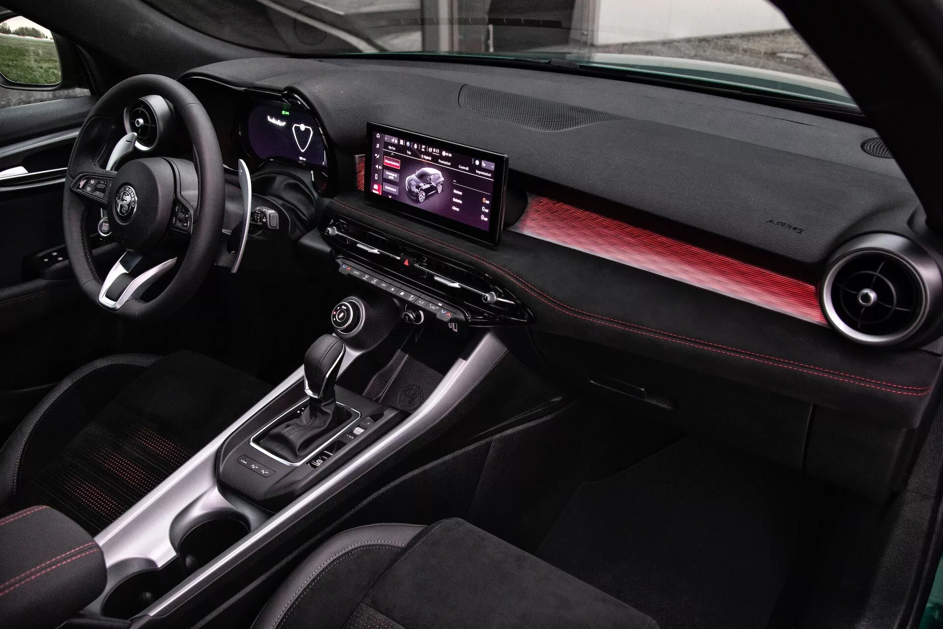 Interiér Alfa Romeo Tonale 2022 se moderním palubním panelem, digitálním informačně-zábavním centrem, akcenty z uhlíkových vláken a sedadly se červeným prošíváním, pohled z perspektivy spolujezdce