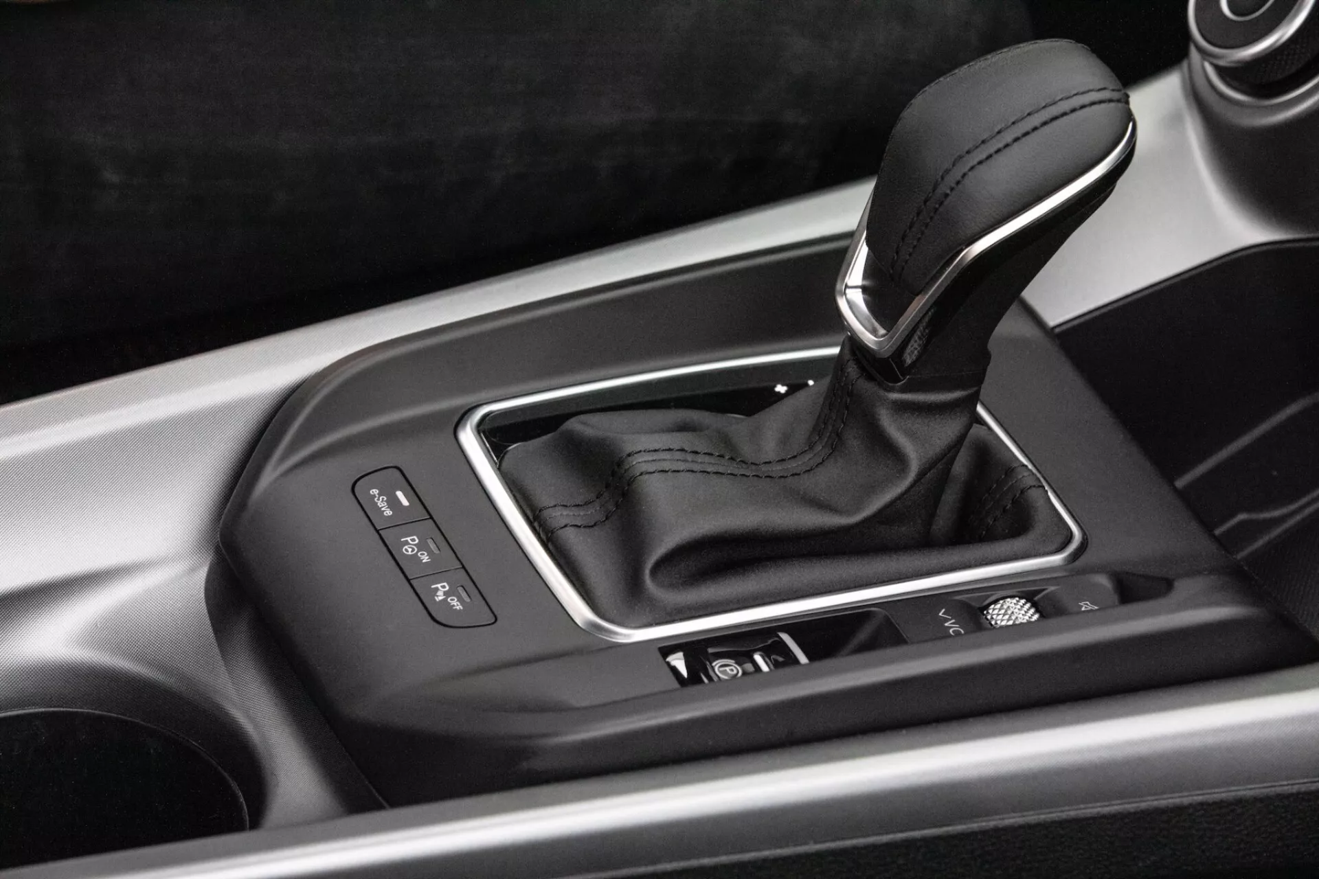 Detailní interiérový pohled na centrální konzoli Alfa-Romeo Tonale 2022 s pákou automatické převodovky ve stříbrném pouzdru s ukazateli volby rychlostí, integrovanými ovládacími tlačítky a vysoce kvalitním provedením
