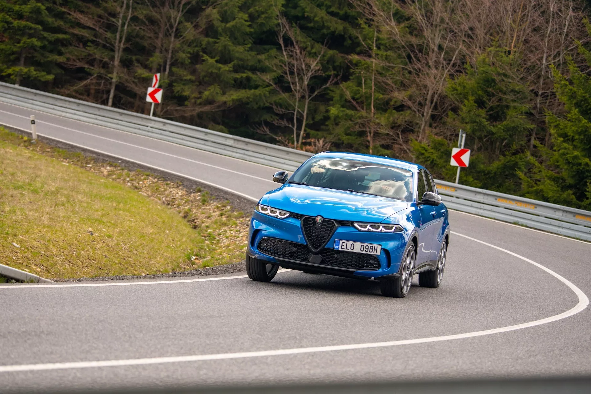 Dynamická jízda Alfa Romeo Tonale 2022 na zakřivené silnici s pohledem na přední čtvrtinu, LED světlomety, charakteristickou mřížku a výkonná kola