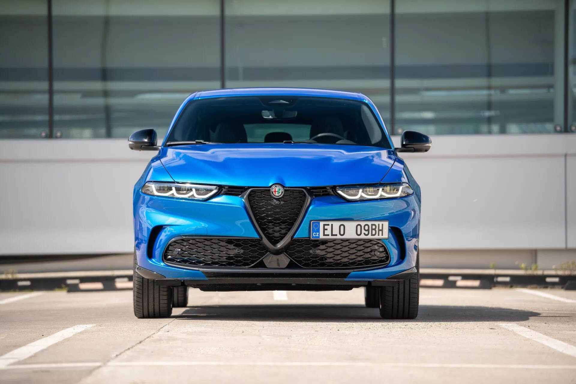 Modrý Alfa Romeo Tonale 2022, pohled zepředu na parkovišti ukazuje masku s emblémem, LED světlomety a aerodynamické prvky designu