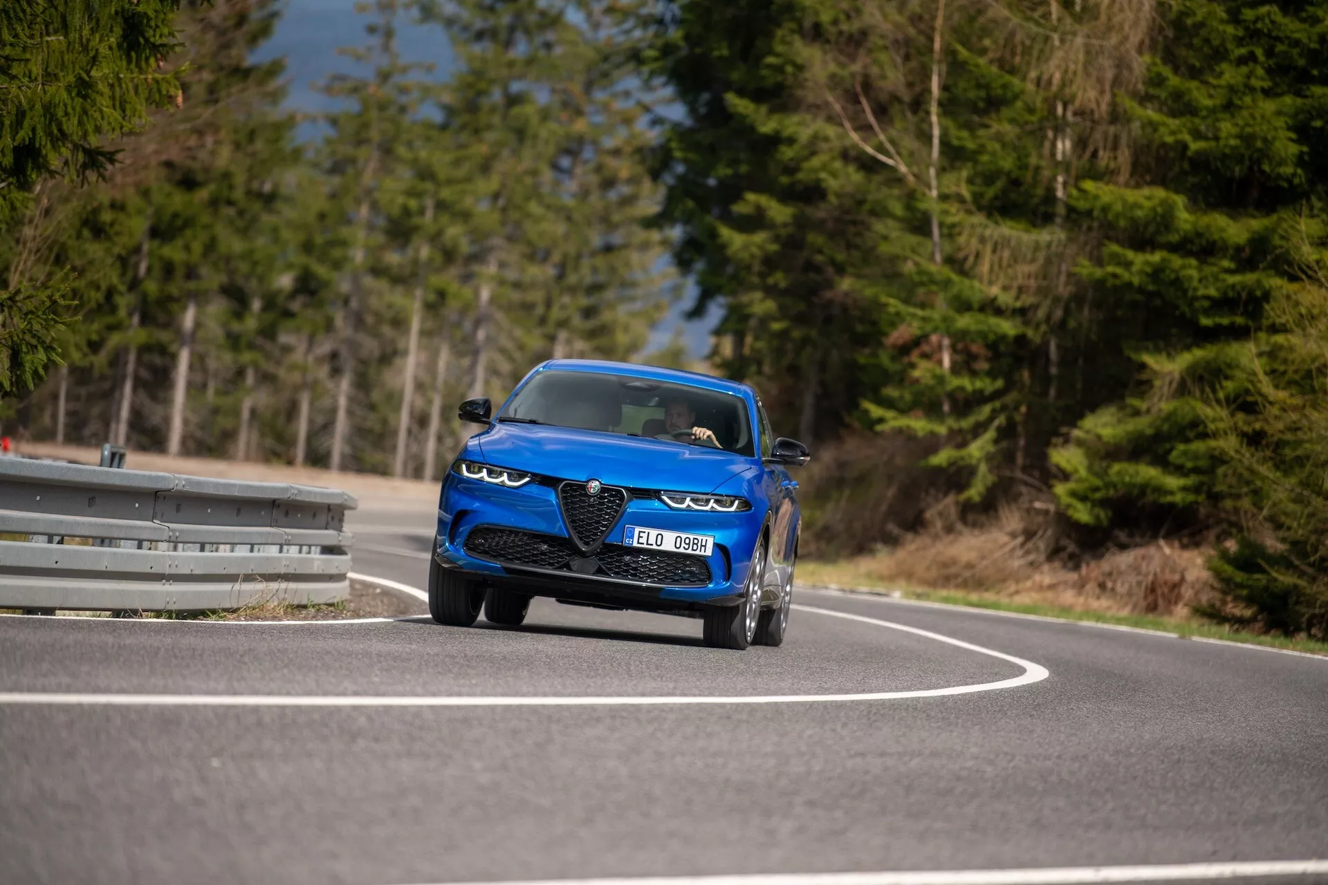 Alfa-Romeo Tonale 2022 v pohybu na zakřivené silnici, zdůrazňující jeho dynamický design, LED světlomety, vzduchové vstupy, sportovně kabrioletový styl a luxusní prvky z nízkého úhlu pohledu ze tří čtvrtin vpředu