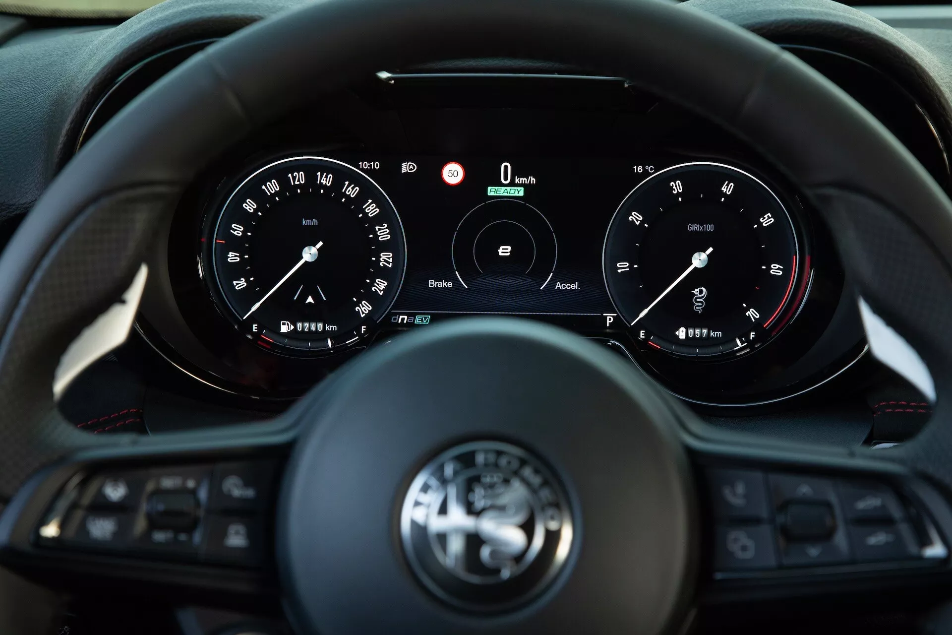 Interiér Alfa Romeo Tonale 2022 ukazující pohled řidiče na tříramenný multifunkční volant a přístrojový panel s analogovými ukazateli a centrálním digitálním displejem ukazujícím nulovou rychlost a otáčky, s funkcemi pro propojení a asistenční systémy řidiče