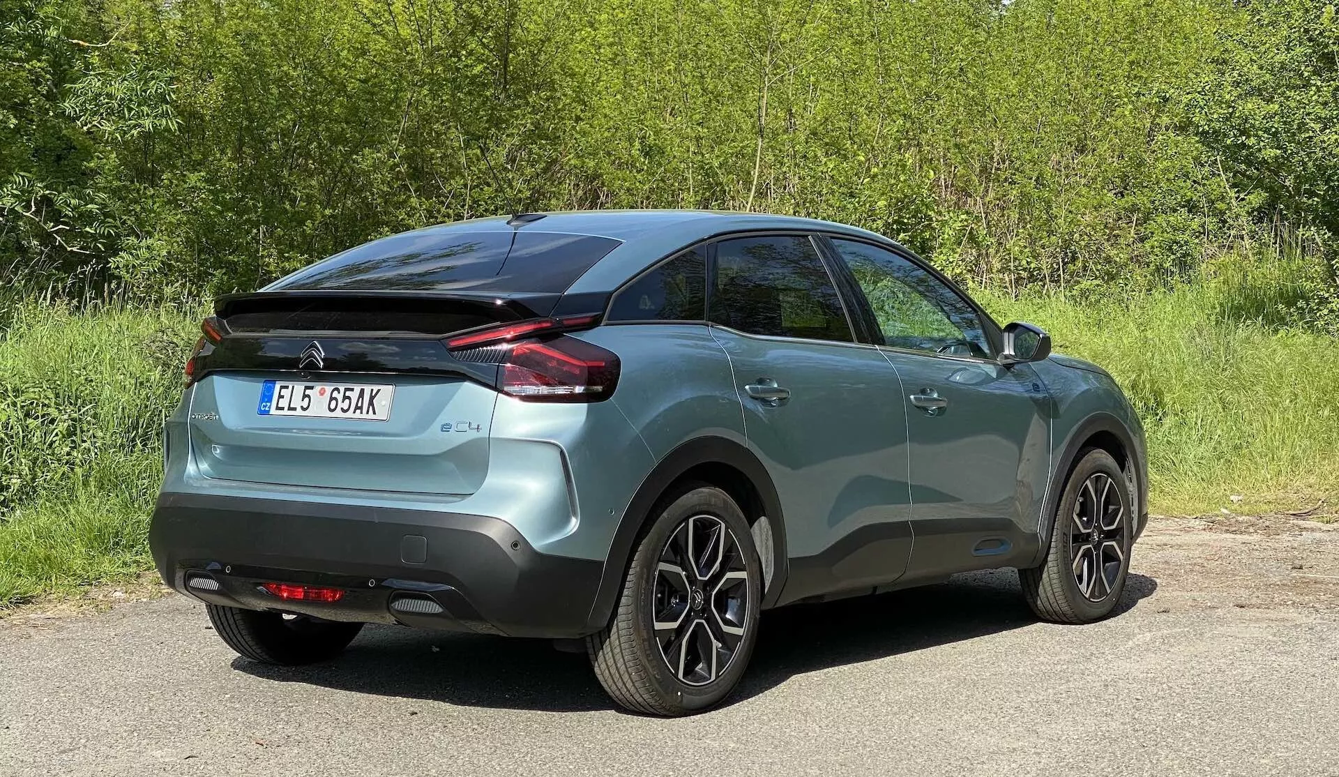Obrázek vozu Citroen C4 2020 (e-C4) zobrazující zadní třičtvrteční úhel. Vozidlo s kovovým lakem je umístěno uprostřed, odhaluje boční a zadní profil, včetně horizontálně navržených zadních světel, kliky dveří v barvě karoserie a vícepaprskových litých kol. Nastavení naznačuje venkovní prostředí s nějakou vegetací v pozadí.