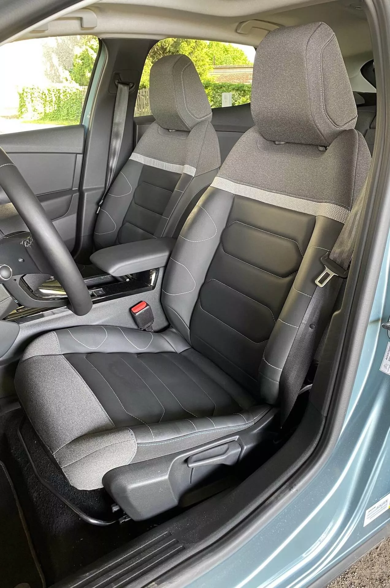 Interiér Citroen C4 2020 (e-C4) s důrazem na řidičovu stranu, záběr z otevřených dveří zobrazující volant, sedadla a část palubní desky s ovladači na volantu.