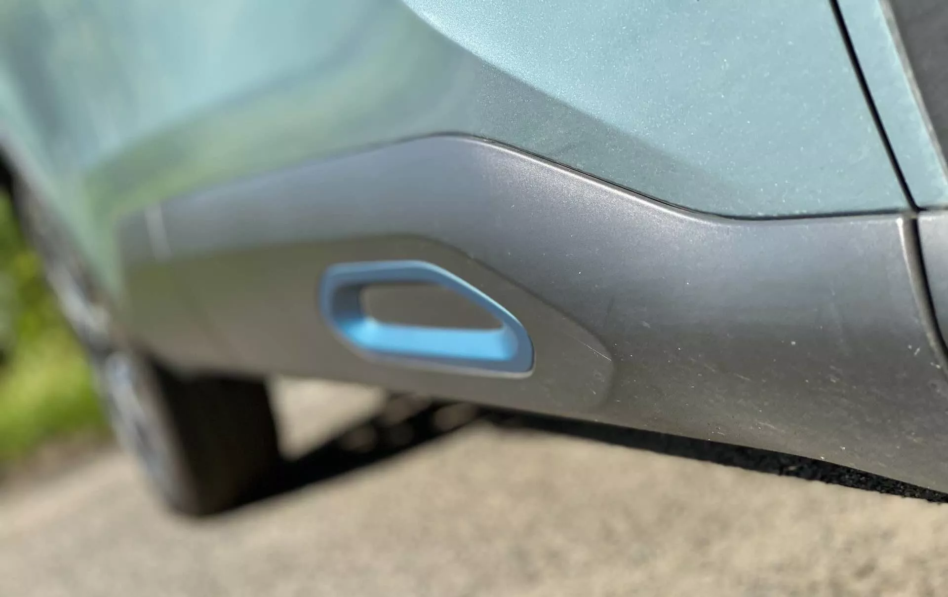 Detailní záběr na boční část vozu Citroen C4 2020 (e-C4) s moderní, aerodynamicky integrovanou klikou dveří. Klika je zarovnaná s panelem dveří a možná osvětlena pro bezklíčový vstup, což naznačuje pokročilý elektronický mechanismus zasouvání nebo vysouvání. Kovový odstín vozu a lesklý povrch jsou zvýrazněny denním světlem a odrazy.