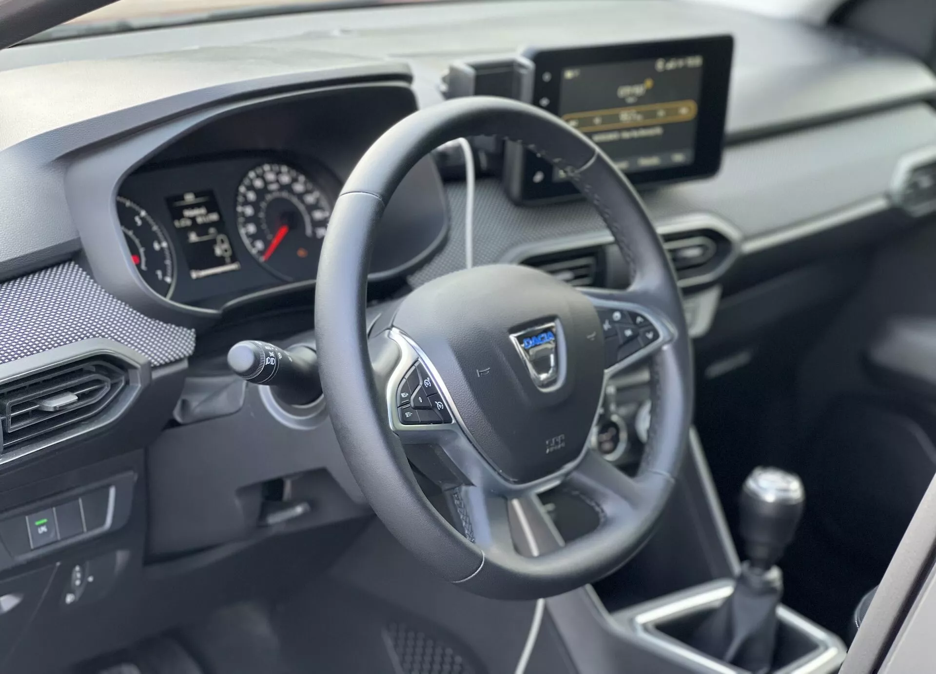 Interiér Dacia Jogger 2022 se zaměřením na oblast řidiče s volantem se třemi rameny s multifunkčními tlačítky, analogově-digitálním přístrojovým panelem, středovou konzolou s infotainment systémem a manuální převodovkou