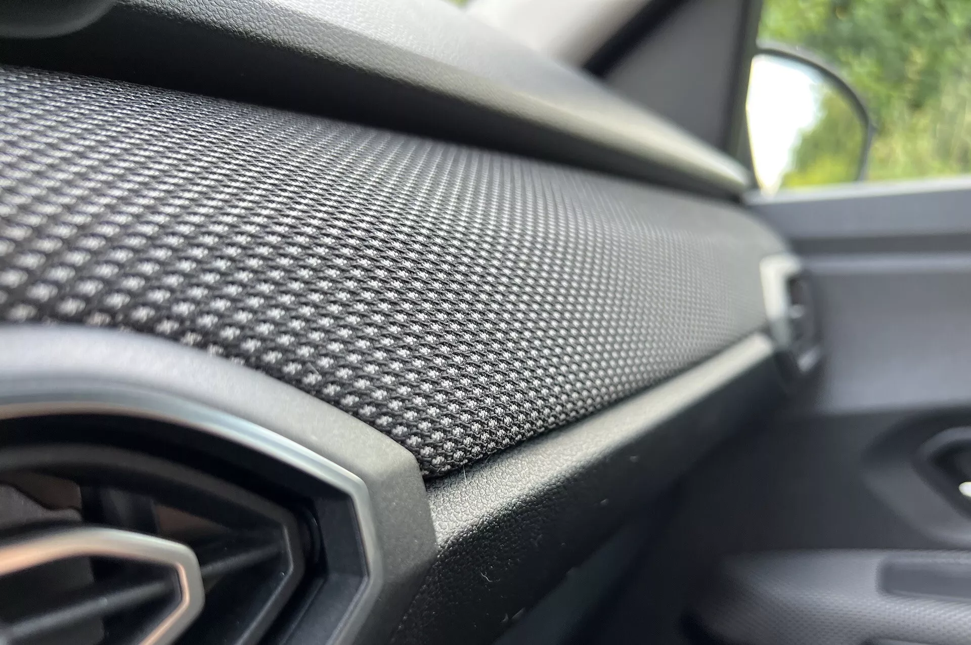 Detailní pohled na palubní desku na straně spolujezdce Dacia Jogger 2022 s vzorem z uhlíkových vláken a větrací mřížkou, zdůrazňující moderní design a luxusní výbavu