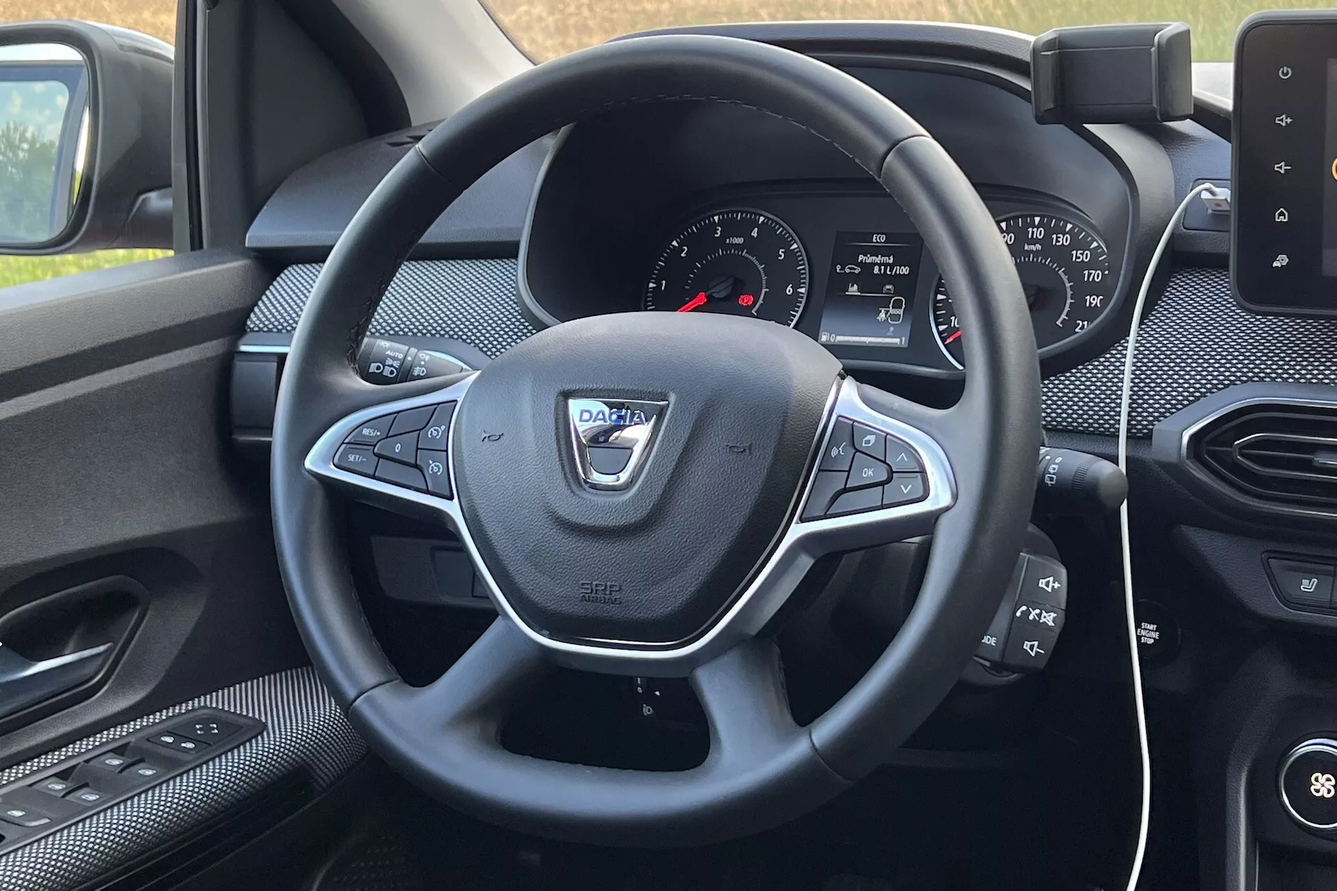 Interiér Dacie Jogger 2022 z pohledu řidiče, zaměřený na volant s multifunkčními ovladači a palubní desku s infotainment systémem