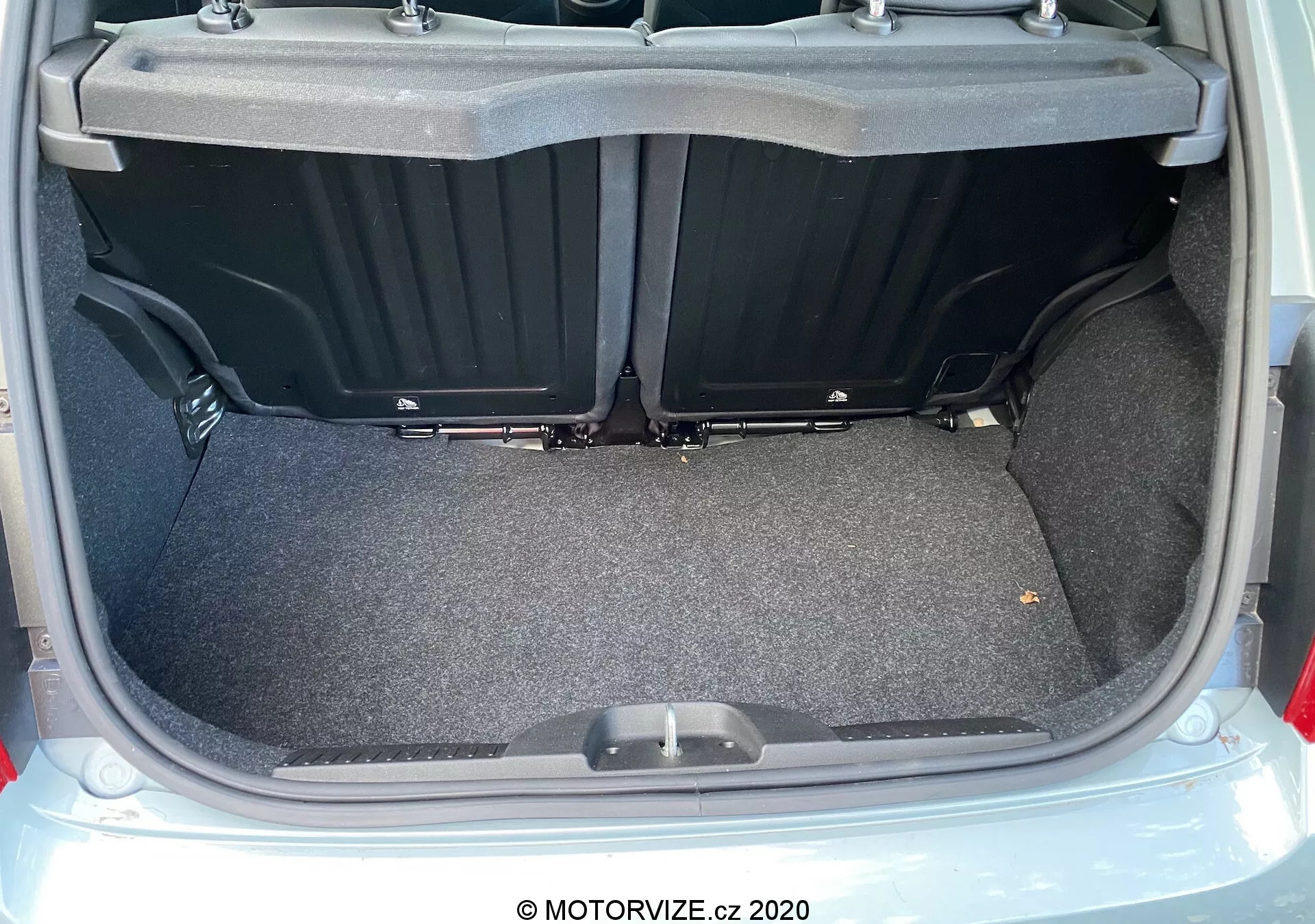 Detailní pohled na zavazadlový prostor Fiat 500 z roku 2015 zezadu s otevřeným víkem, zobrazující kobercem pokrytý, plochý nákladový prostor s plastovými bočními přihrádkami a madlem na podlaze kufru. Obrázek zdůrazňuje prostornost, využitelnost a čistý, dobře osvětlený stav kufru.