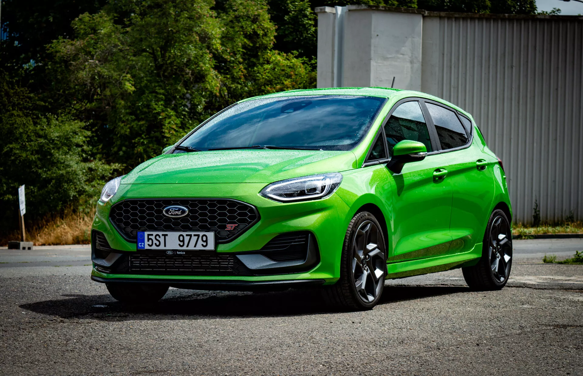Živě zelený hatchback Ford Fiesta 2022 ve tříčtvrtečním předním pohledu zobrazující přední mřížku se znakem, sportovní nárazník s mlhovými světly, ostrá úhlová světlomety, aerodynamické kontury, velká černá slitinová kola a moderní systém osvětlení