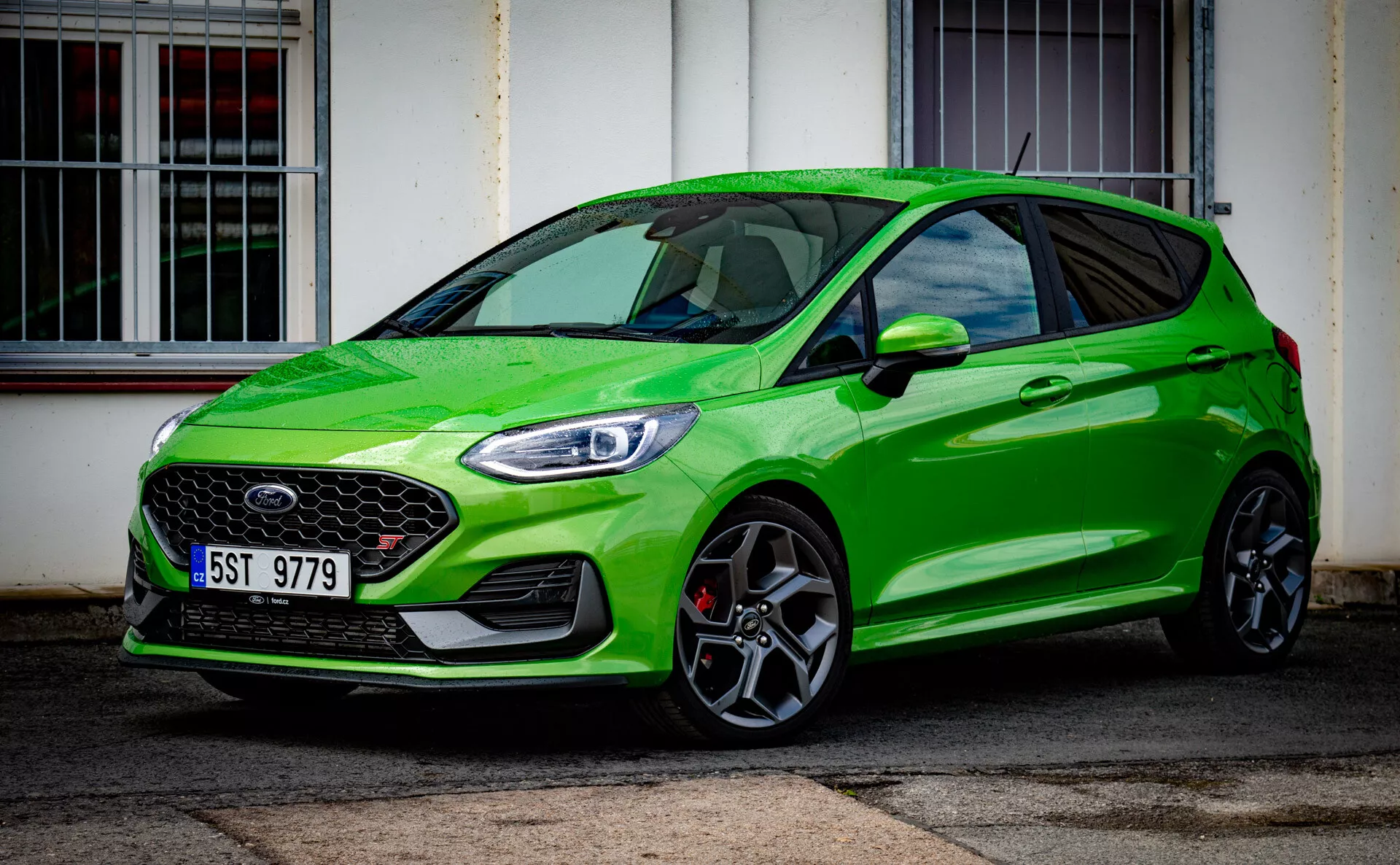 Světle zelený Ford Fiesta moderního modelu hatchback z roku 2022 zdůrazňující sportovní postavu s výraznou přední mřížkou a elegantními LED světlomety, parkovaný šikmo před budovou