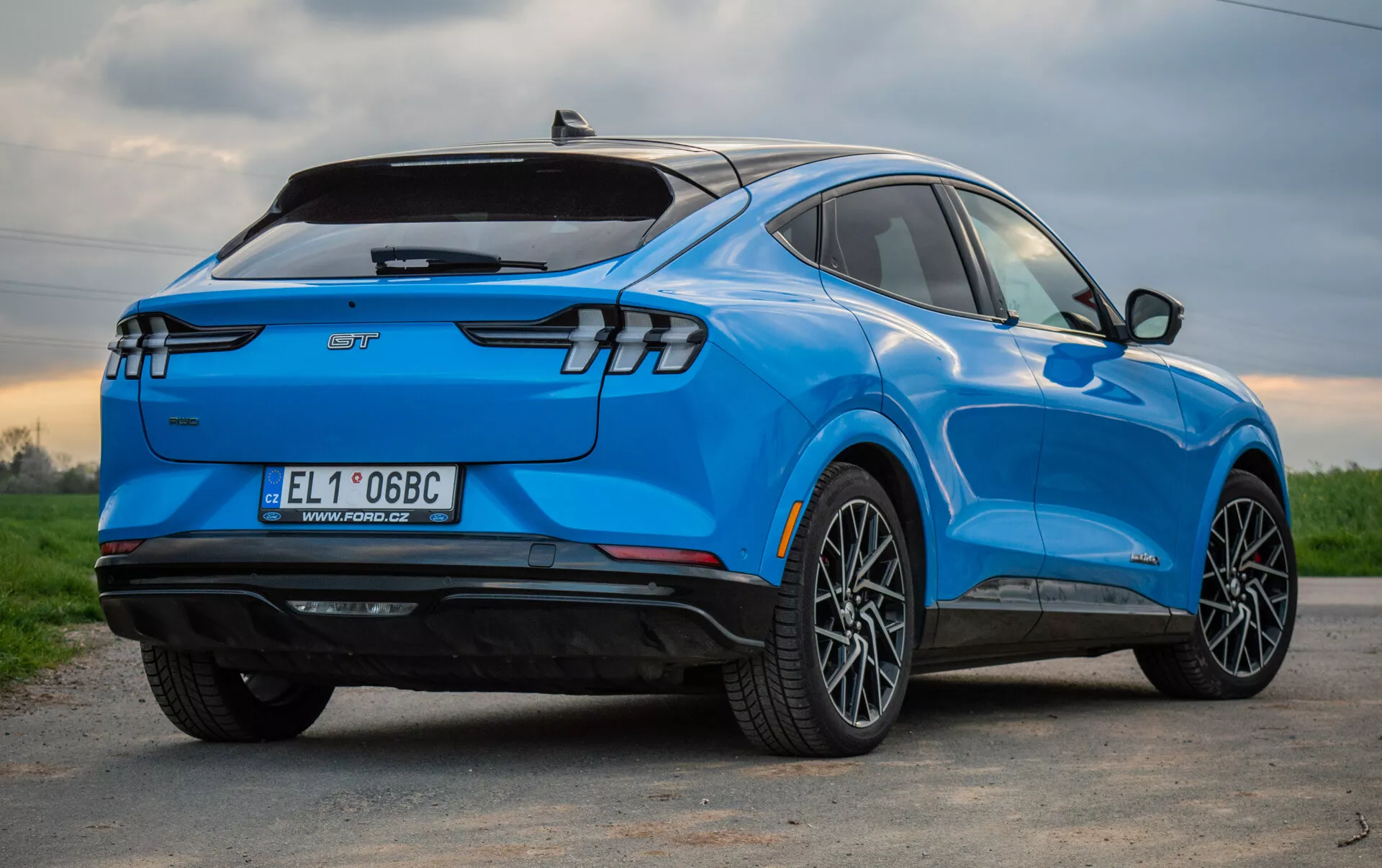 Modré elektrické SUV Ford Mustang Mach-E 2020 zobrazené z trojčetné zadní perspektivy, zdůrazňující jeho stylový aerodynamický design, moderní zadní LED světla, slitinová kola s více paprsky, označení elektrického vozidla a technologické vlastnosti