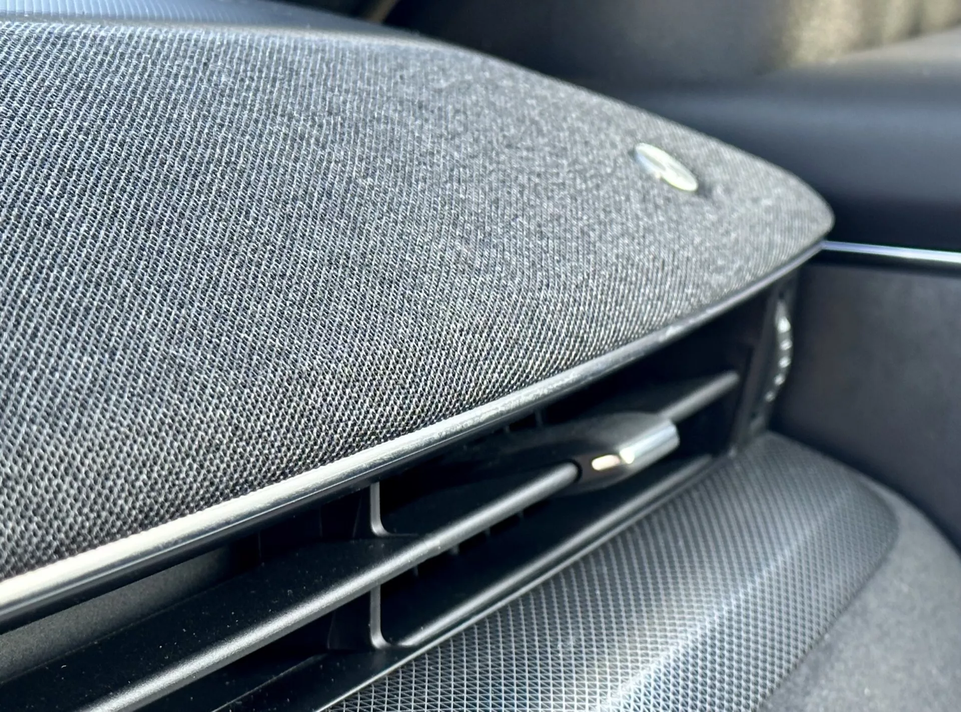 Detailní pohled do interiéru Ford Mustang Mach-E 2020 ukazující část palubní desky nebo dveřního panelu s integrovanou mřížkou reproduktoru z prémiové tkaniny, emblémem naznačujícím partnerství s výrobcem high-end audio techniky, spolu s lesklým černým vzduchovým ventilem