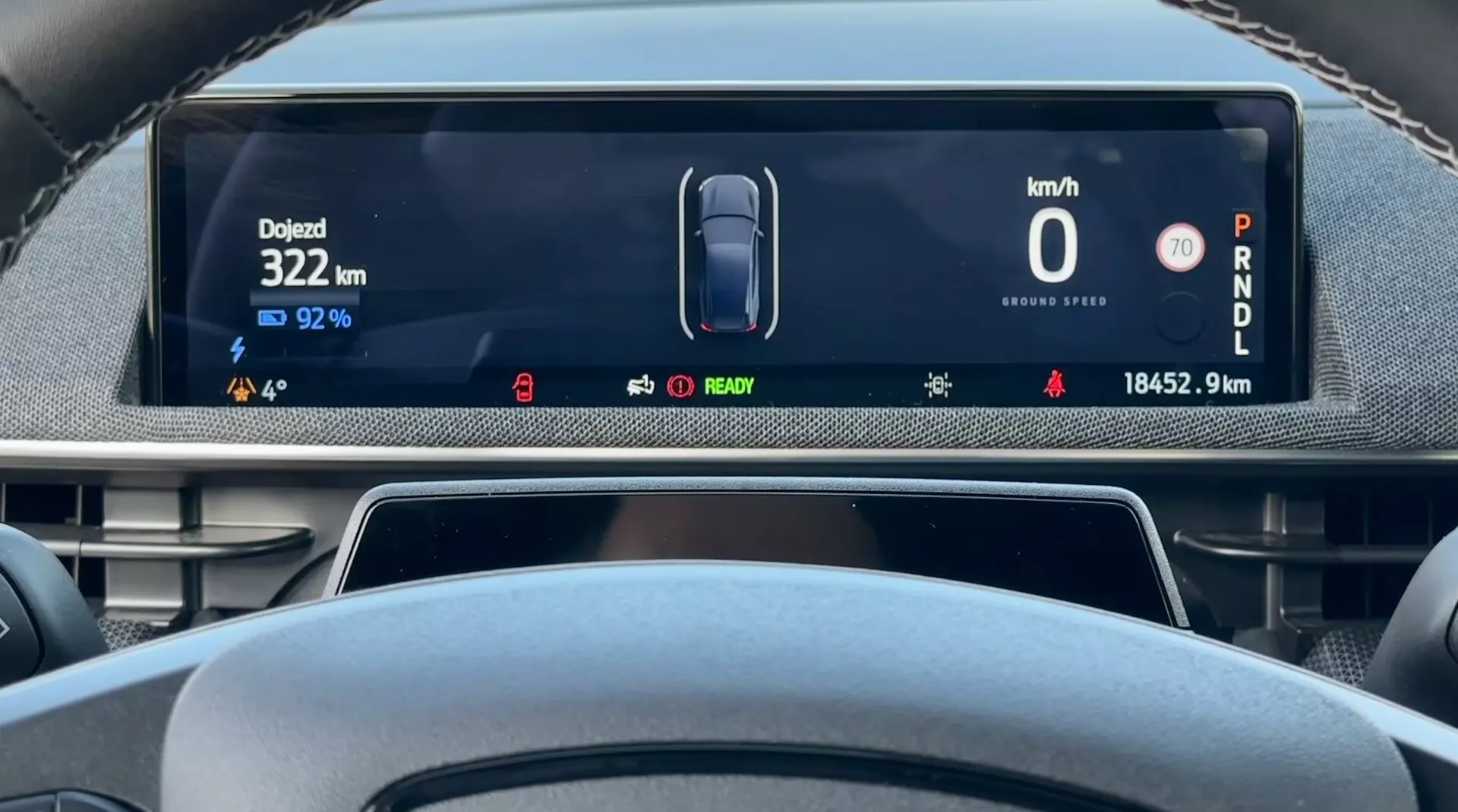 Digitální panel přístrojů Ford Mustang Mach-E z roku 2020 z pohledu řidiče zobrazující rychlost vozidla 0 km/h, zbývající nabití baterie 92%, celkovou ujetou vzdálenost 18452,9 km a auto v režimu parkování, s indikátory pro stav elektrického vozidla a pokročilými asistenčními systémy pro řidiče
