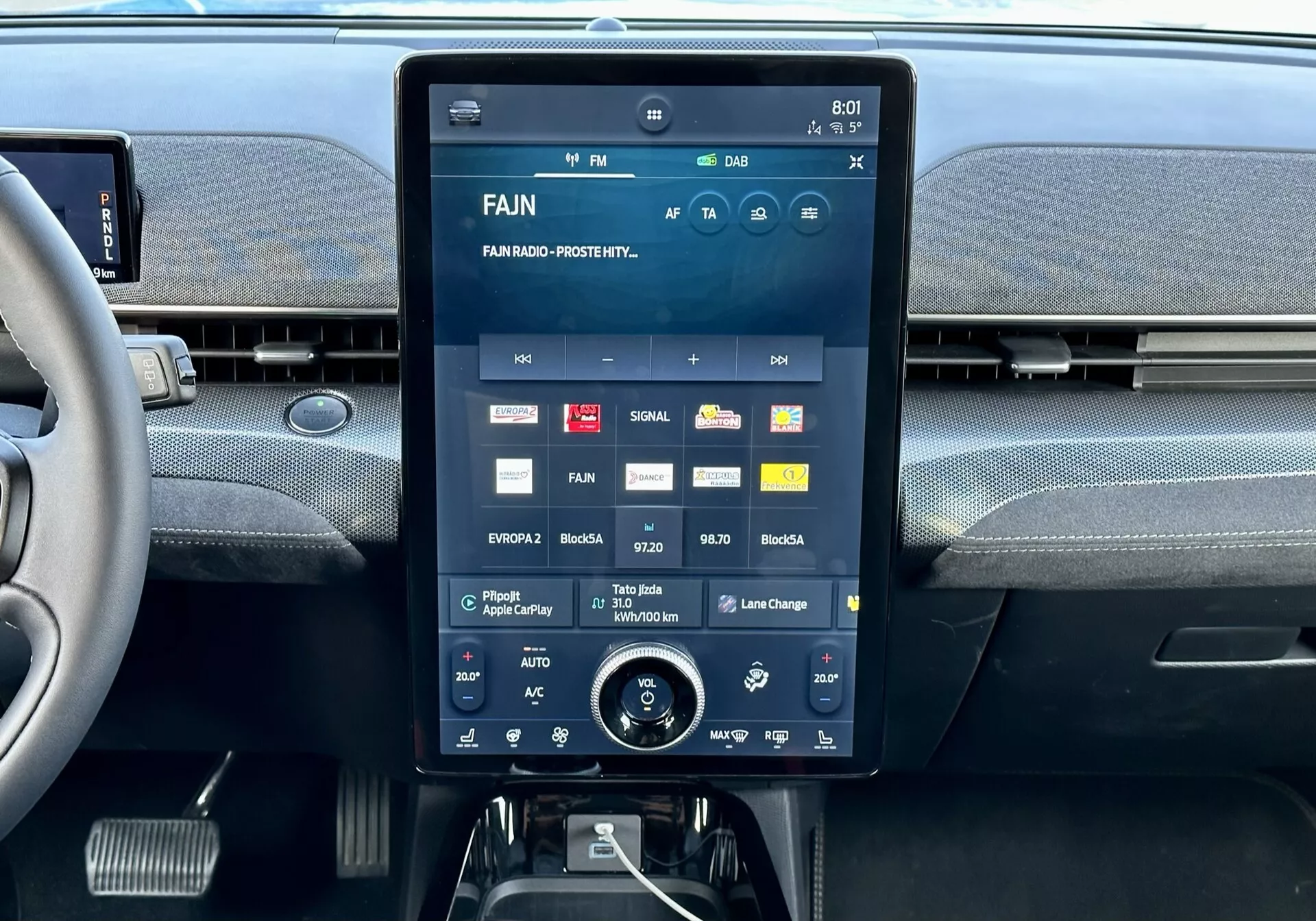 Interiérová centrální konzole Ford Mustang Mach-E 2020 s velkým dotykovým displejem zobrazujícím multimediální rozhraní s aplikacemi a nastaveními, integrované výdechy vzduchu nahoře a další otočný ovladač klimatizace dole.