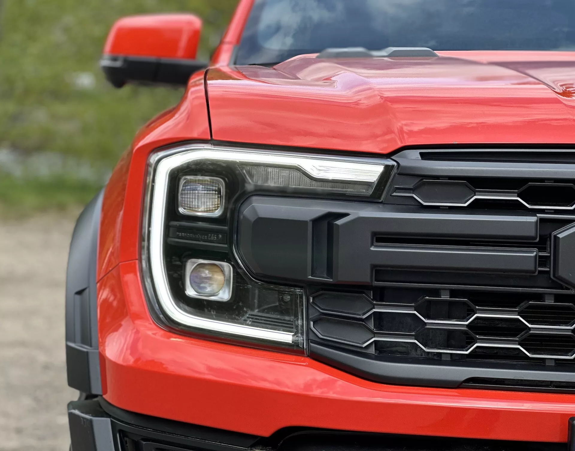 Detailní pohled na přední roh Fordu Ranger 2022 s šestiúhelníkovou mřížkou, detailním světlometem a profilovanou kapotou v červené barvě