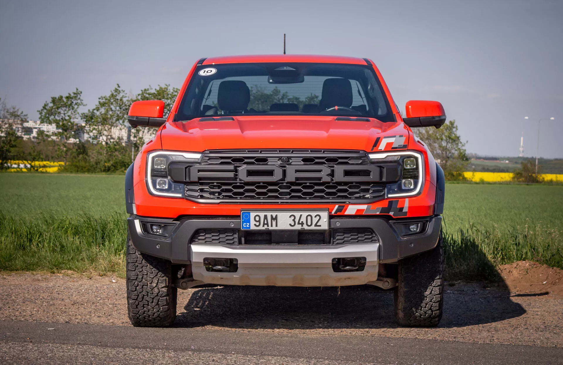 Přední pohled na červený pickup Ford Ranger 2022 na asfaltu s pozadím čisté oblohy, se zaměřením na mřížku, LED světlomety, přední nárazník s háky na tažení a ochranným plechem a logem Ford