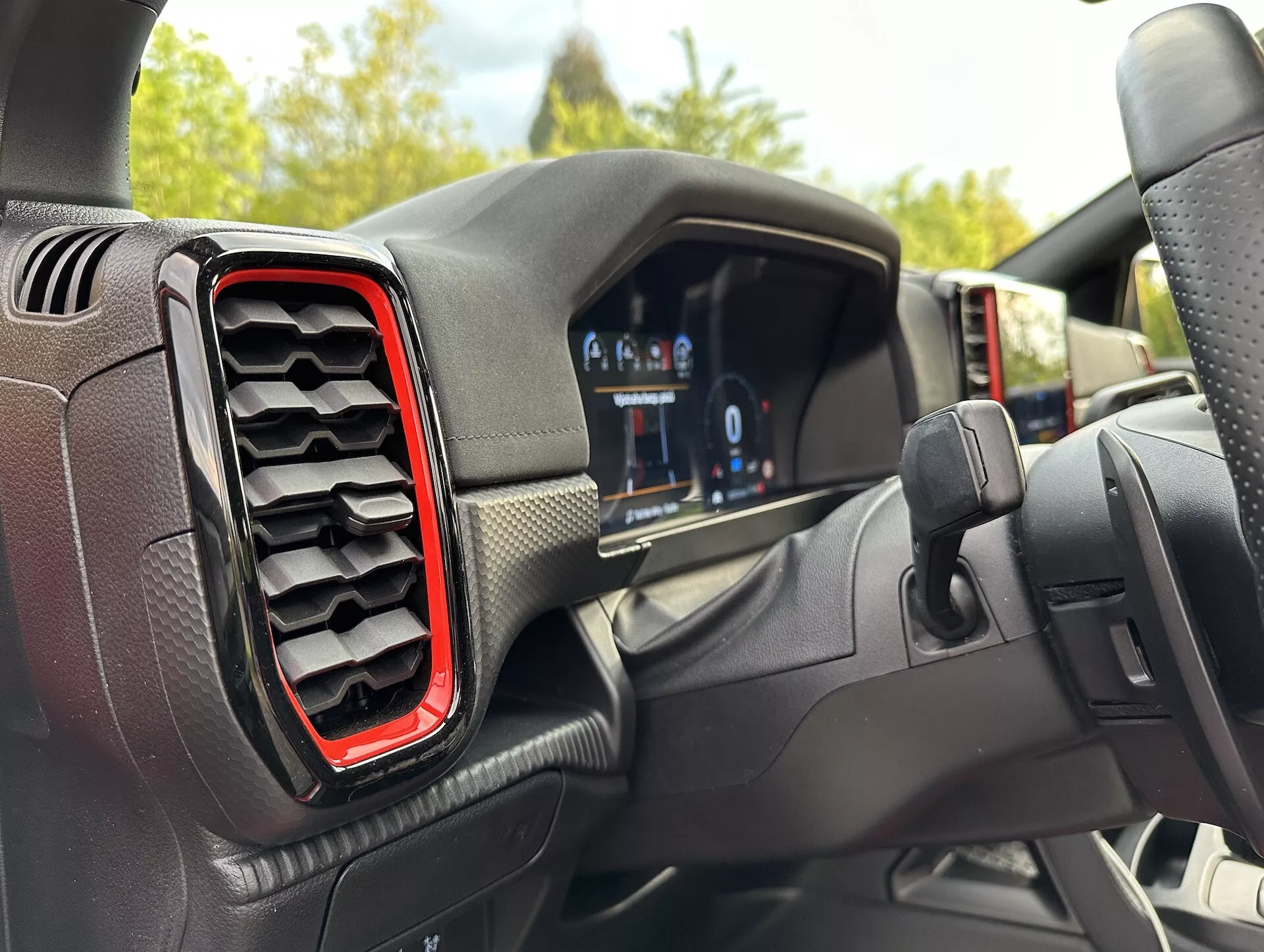 Interiér Ford Ranger 2022 z pohledu řidiče, s digitálním přístrojovým panelem a červeně zvýrazněným levým ventilačním otvorem, s mírně excentrickým úhlem směrem k volantu naznačujícím otáčení