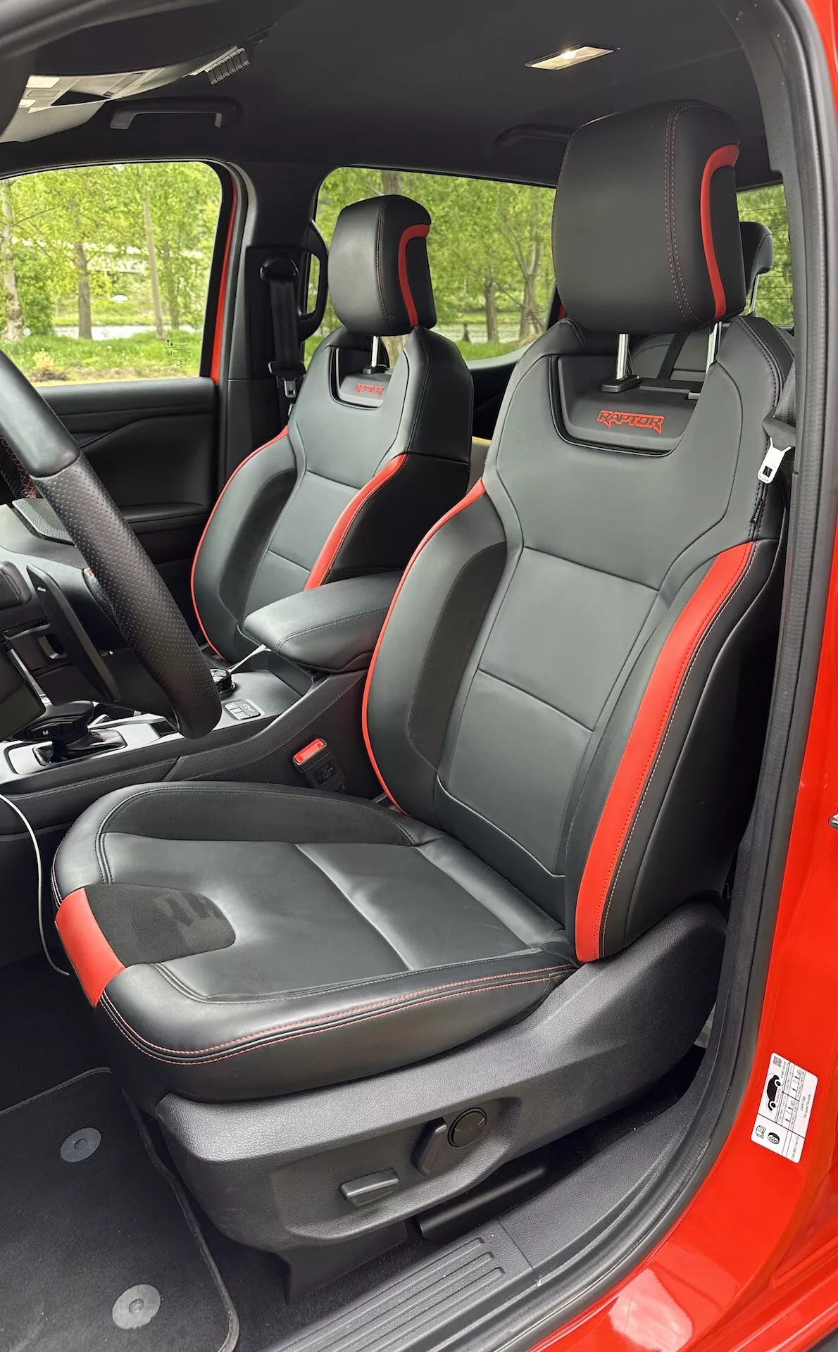 Interiérový pohled na Ford Ranger 2022 zaměřený na sportovní přední sedadla s černým a červeným dekorativním lemem, integrovanými funkcemi opěrek hlavy a elektrickými nastaveními sedadel z perspektivy z pravé strany