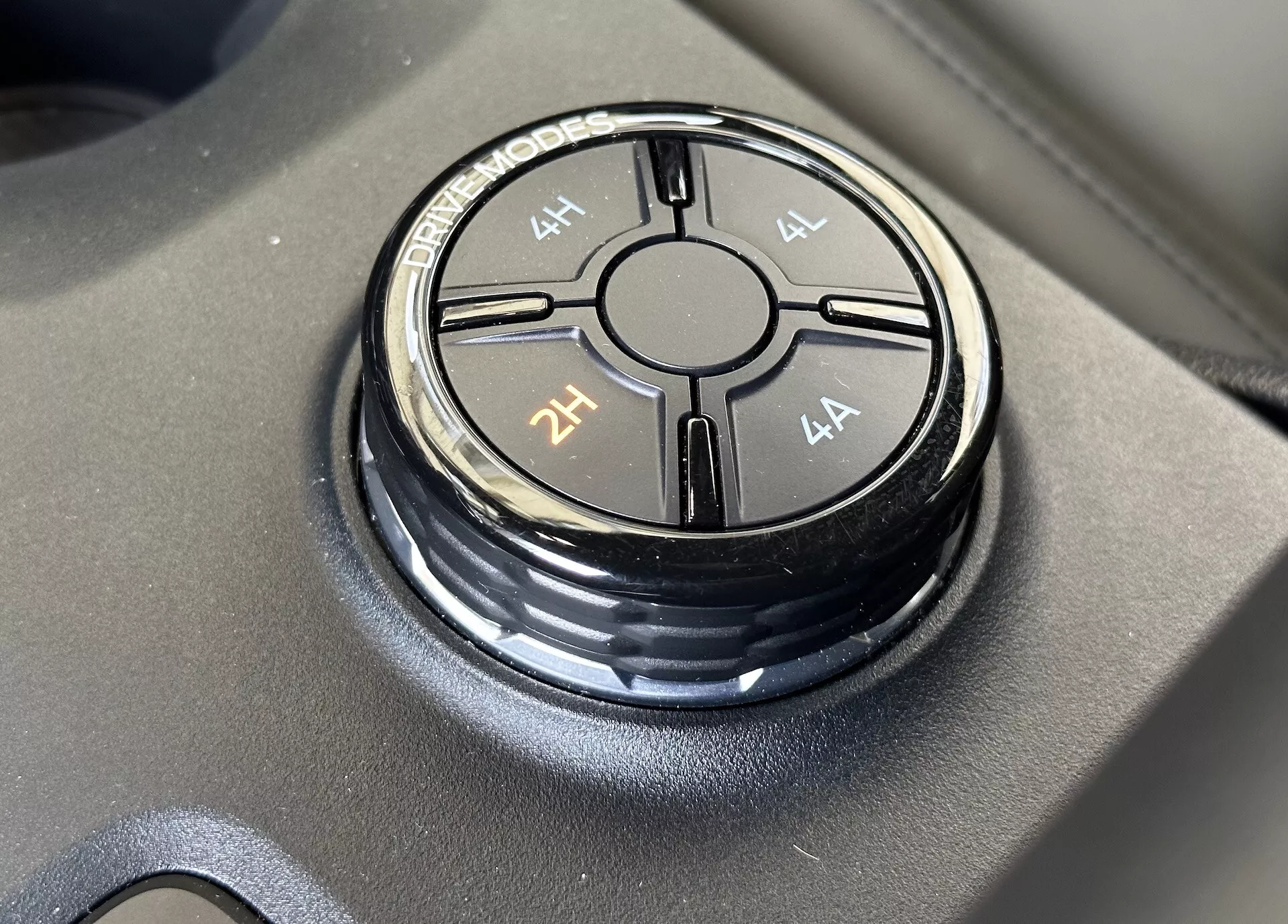 Detailní pohled na volič režimu jízdy Ford Ranger 2022 umístěný na matně černém povrchu, zobrazující možnosti režimů jízdy 4L, 4H, 2H a 4A s ostrým zaostřením a jemným odleskem