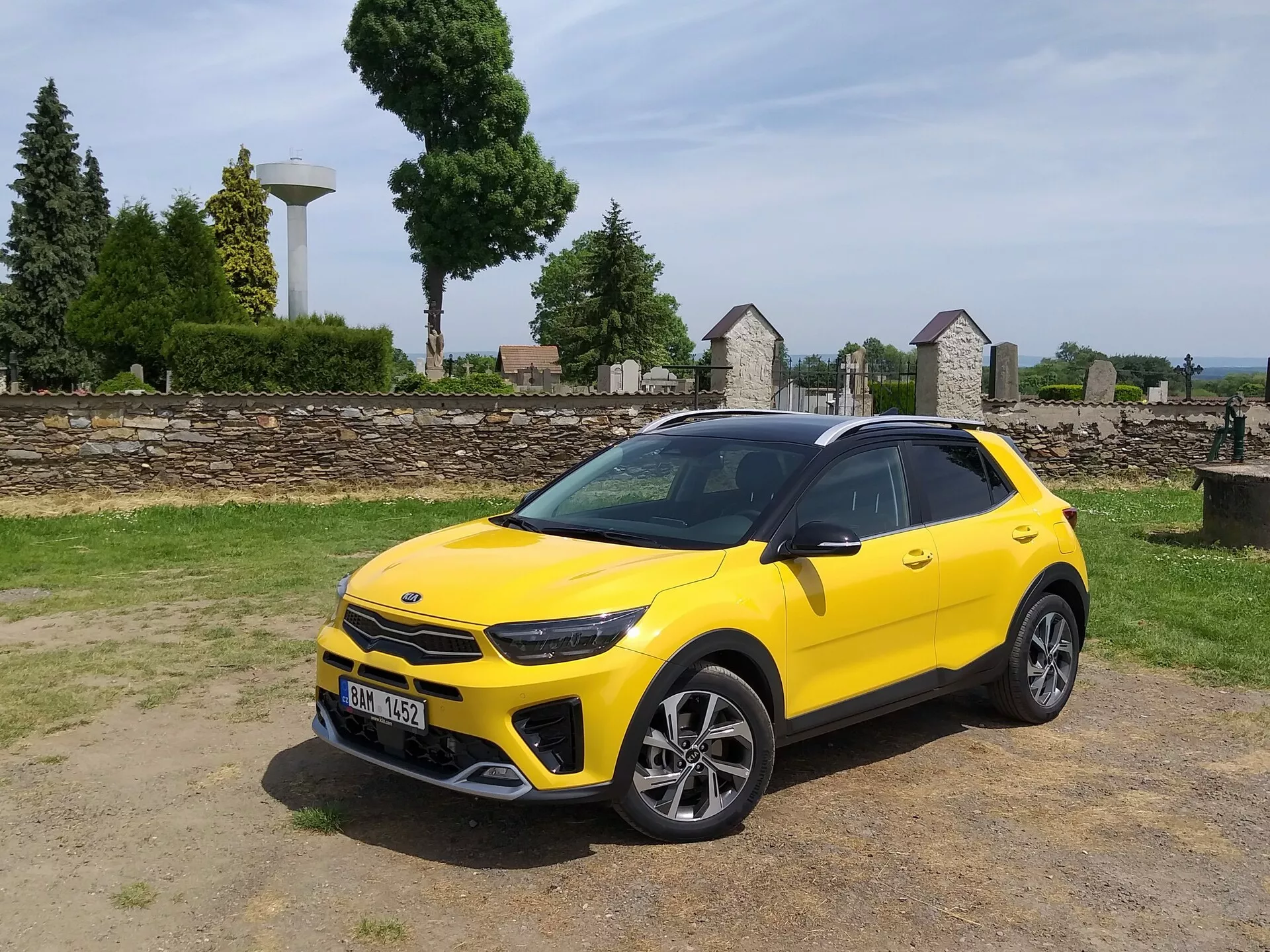 Kia Stonic 2017 v jasně žluté barvě, prezentující svou přední mřížku, LED světlomety, sportovní přední nárazník a elegantní boční profil s vícepaprskovými slitinovými koly a střešními nosiči, což zdůrazňuje estetiku kompaktního crossoveru a pokročilé designové prvky vozidla.