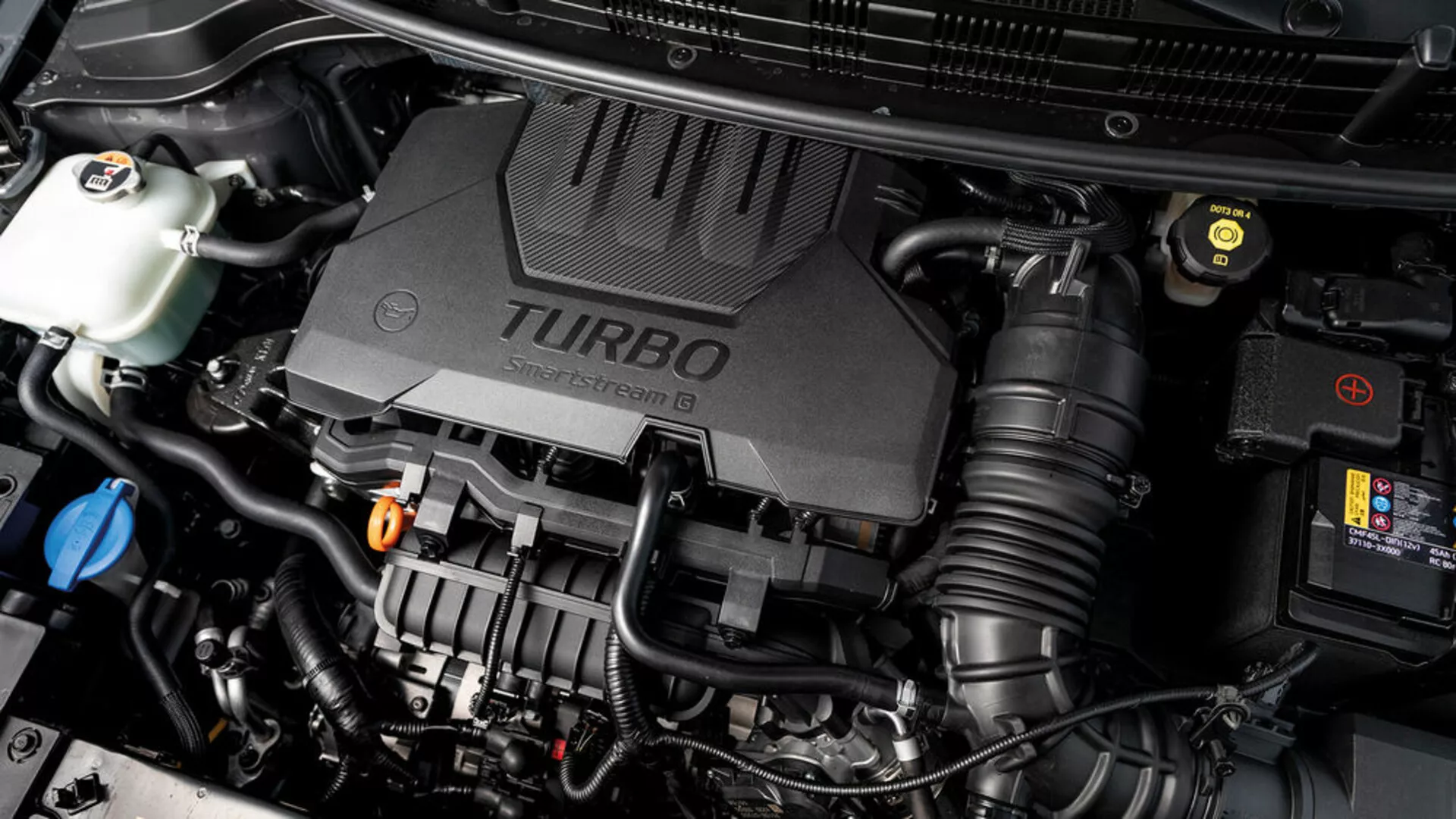 Detailní pohled na motorový prostor Kia Stonic 2017 s krytem turbodmychadlového motoru a různými viditelnými mechanickými součástkami, které předvádějí technologické aspekty vozidla