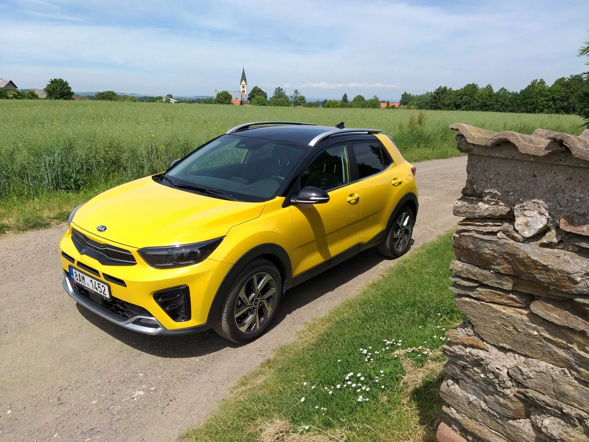 Světle žlutý kompaktní SUV Kia Stonic 2017 s černou střechou, předvádějící svůj elegantní design a dynamické kontury z úhlu tří čtvrtin na venkovské prašné cestě