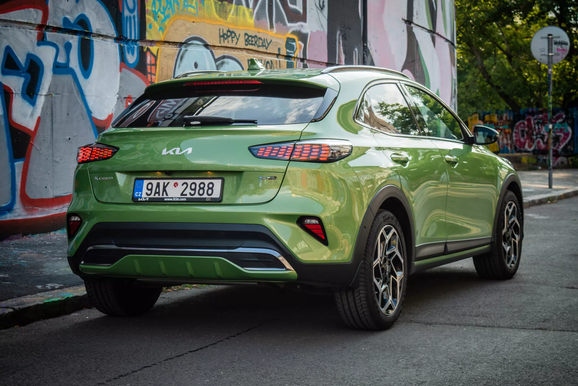 Kia XCeed 2022 ve výrazné zelené barvě ukazuje svůj zadní tříčtvrteční úhel s evropskou SPZ, LED zadními světly, slitinovými koly a městským pozadím.