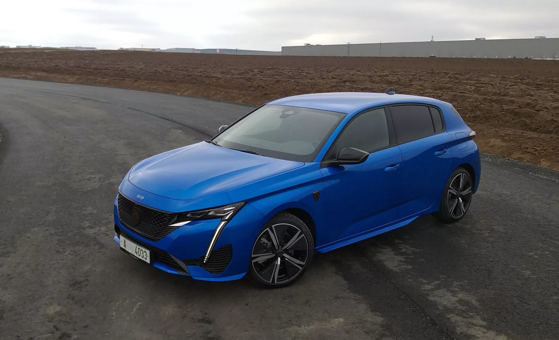 Peugeot 308 hatchback 2022 v jasně modré barvě, s aerodynamickým designem, LED světlomety, pokročilou přední mřížkou, slitinovými koly s více paprsky a moderními bezpečnostními prvky, parkovaný na asfaltu