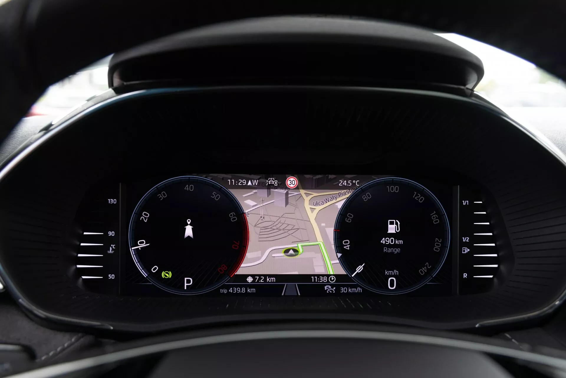 Detailní pohled na moderní přístrojovou desku vozu Škoda Fabia 2021 z pohledu řidiče, s analogovým rychloměrem, velkým digitálním displejem s navigační mapou a digitálním otáčkoměrem. Displeje ukazují 11:29 PM, 24,5°C, dojezd vozu 490 km, aktuální rychlost 0 km/h a údaje o cestě. Kombinuje tradiční a moderní design s pokročilými technologiemi včetně navigace v reálném čase, informací pro řidiče a indikátorů konektivity.