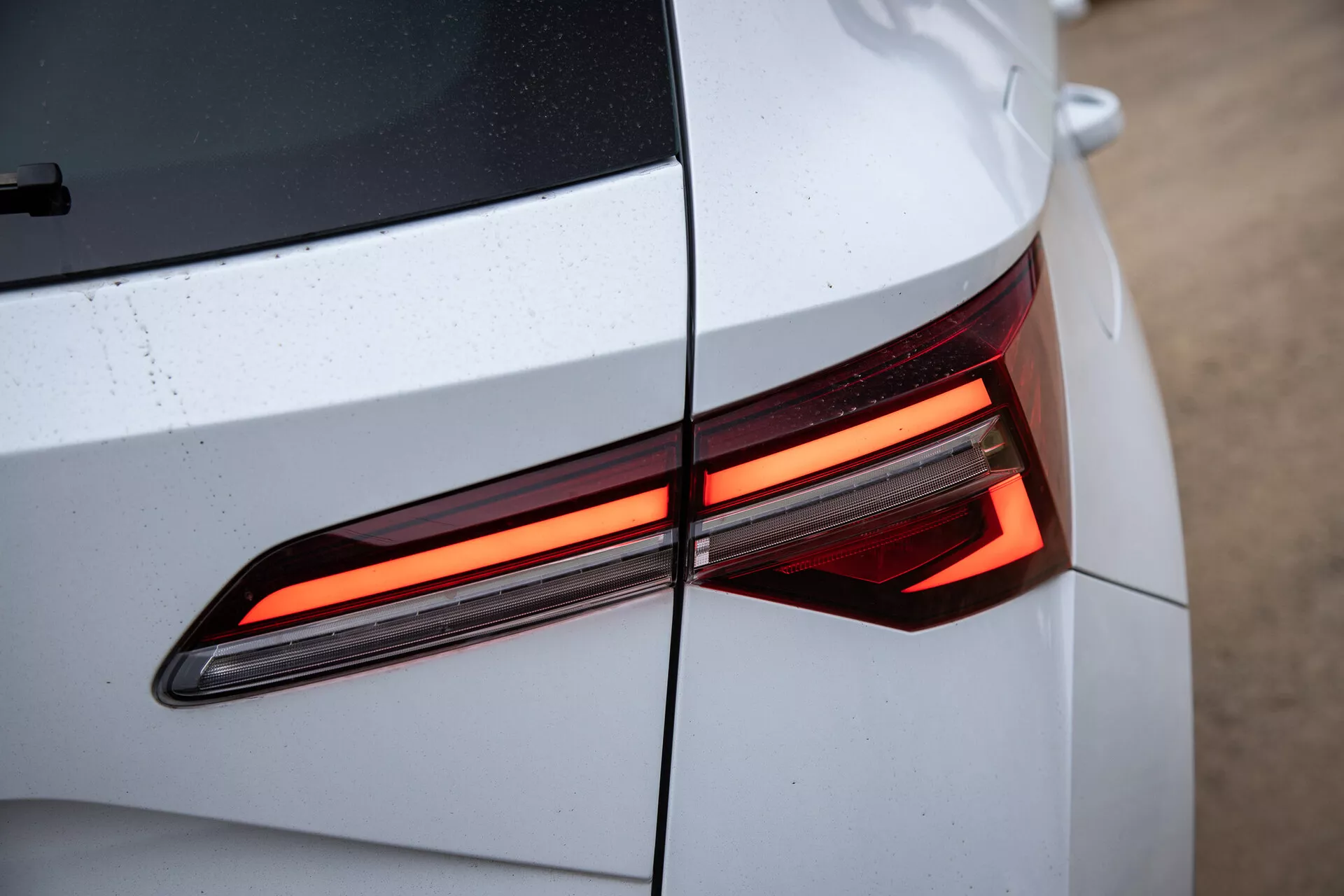 Detailní pohled na zadní část Škody Karoq 2021 ukazující moderní design LED zadního světla, s důrazem na úhlové linie a lesklou, světlou barvu karoserie s viditelnými kapkami vody
