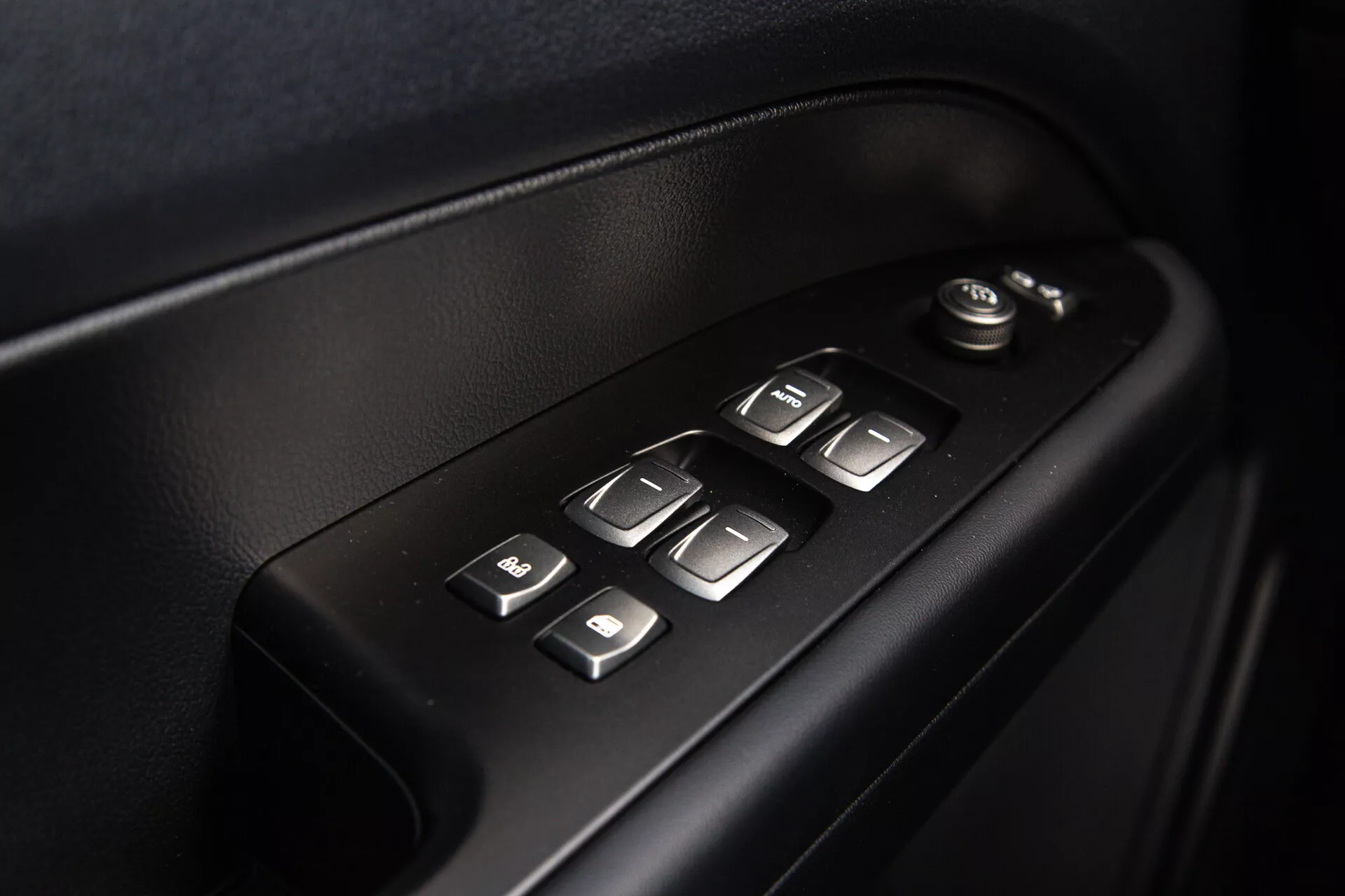 Detailní pohled na ovládací prvky dveří interiéru SsangYong Musso 2022 zobrazující elektrické ovládání oken a zrcátek, osvětlené tlačítka pro snadné použití v ergonomickém designu vysoké kvality