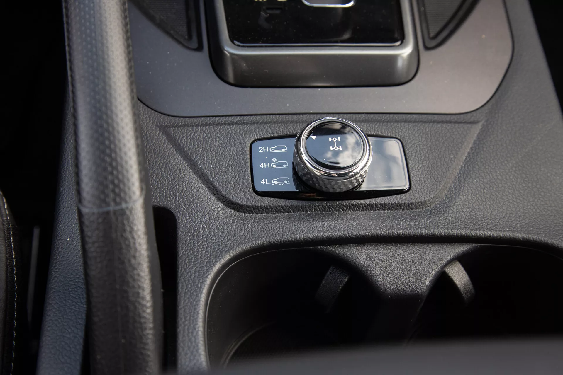 Detailní pohled na středovou konzolu SsangYong Musso 2022 se zaměřením na ovladač 4WD nastavený na 2H, zahrnující moderní design interiéru a užitné funkce