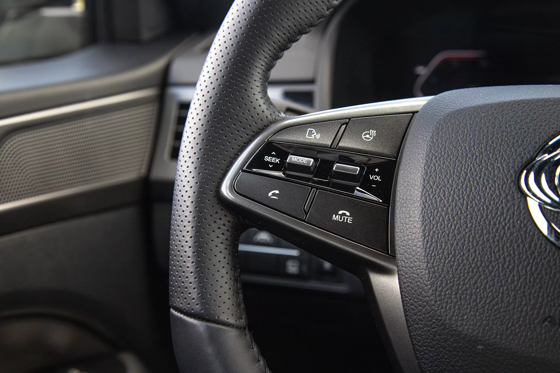 Detailní pohled na ovládací prvky na levé straně volantu SsangYong Musso 2022, včetně perforovaného koženého potahu a tlačítek technologií pro pohodlí a bezpečnost řidiče
