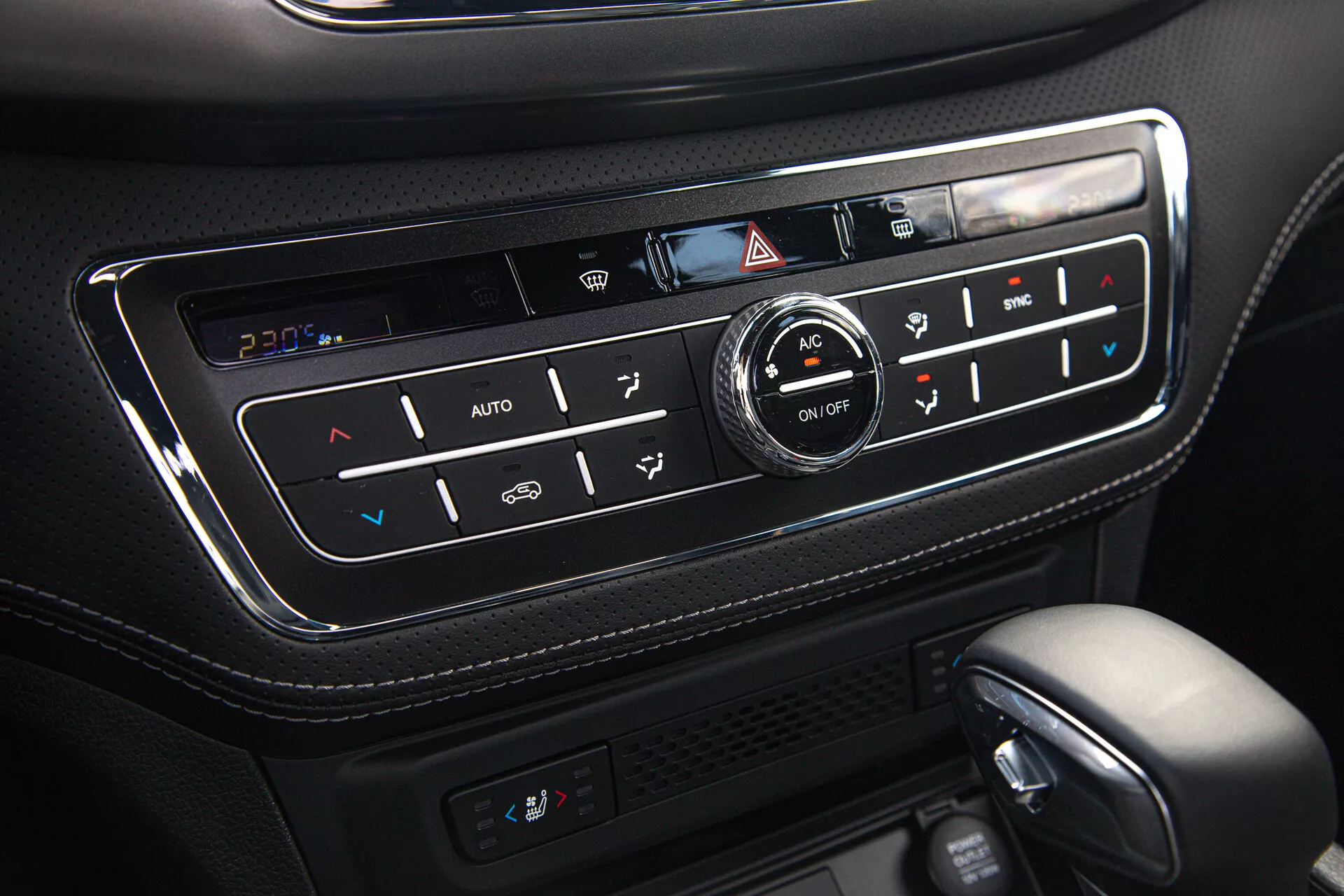 Detailní pohled na panel klimatizace SsangYong Musso 2022 Grand Pick-up s automatickým nastavováním teploty, duálním ovládáním klimatizace, funkcí vyhřívaných sedadel, nastavením AC a odmrazování, umístěný v konzole z vysoce kvalitní černé kůže s lesklým povrchem a podsvícenými tlačítky