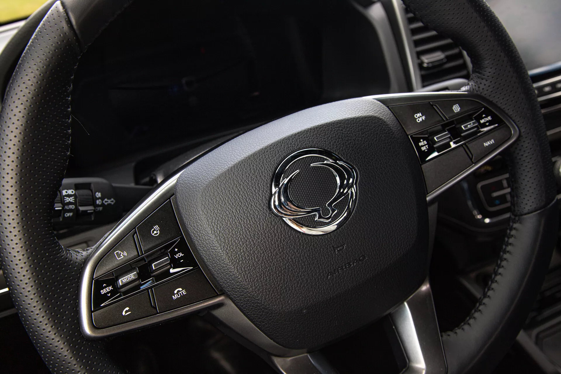 Detailní pohled na volant pick-upu SsangYong Musso Grand 2022 s koženým obšitím, chromovými akcenty a pokročilými ovládacími tlačítky
