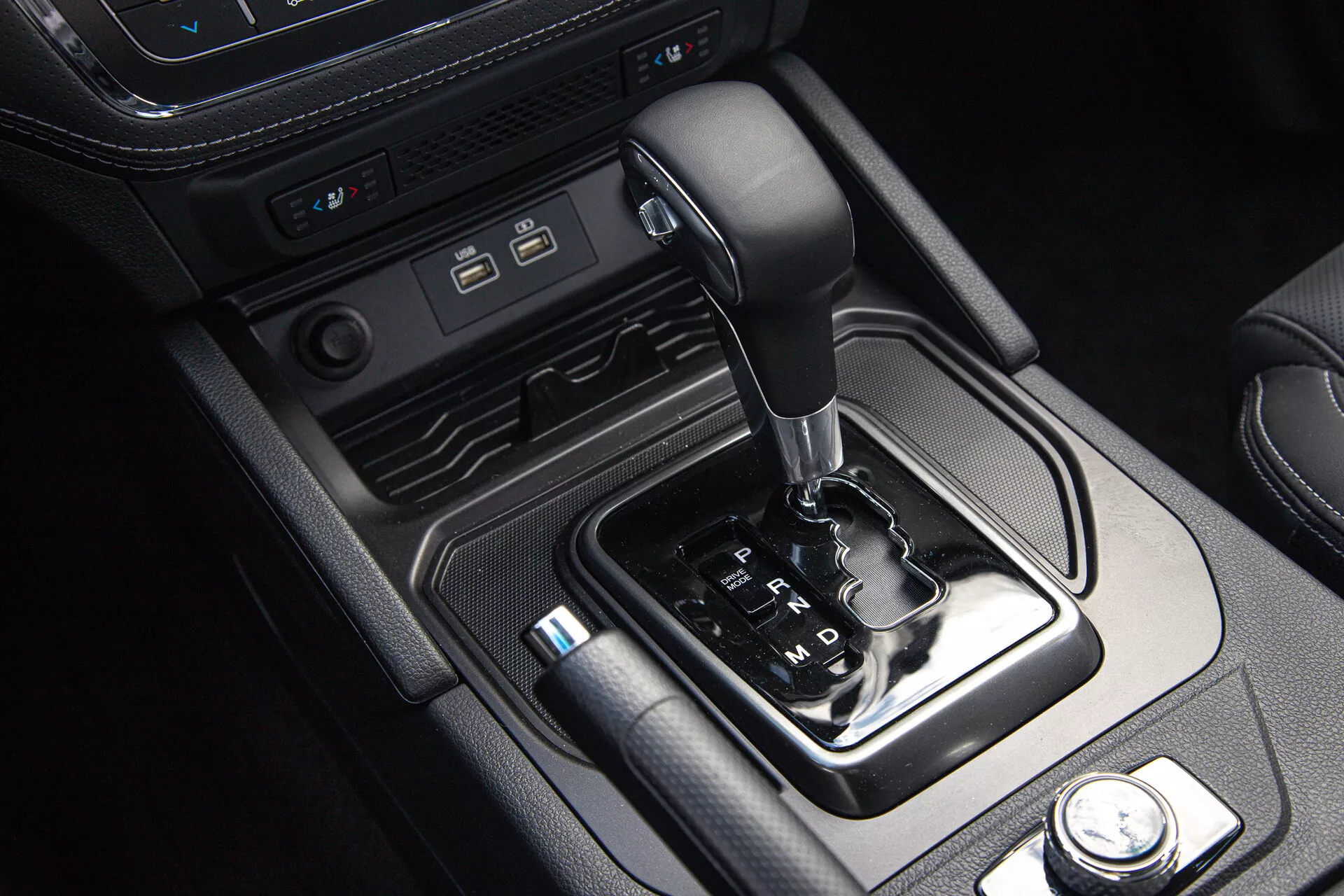 Interiér SsangYong Musso Grand Pickup 2022 s centrální konzolou se selektorem automatické převodovky, moderními porty pro připojení a ovládáním jízdních režimů, orámovaný koženými a kovovými prvky