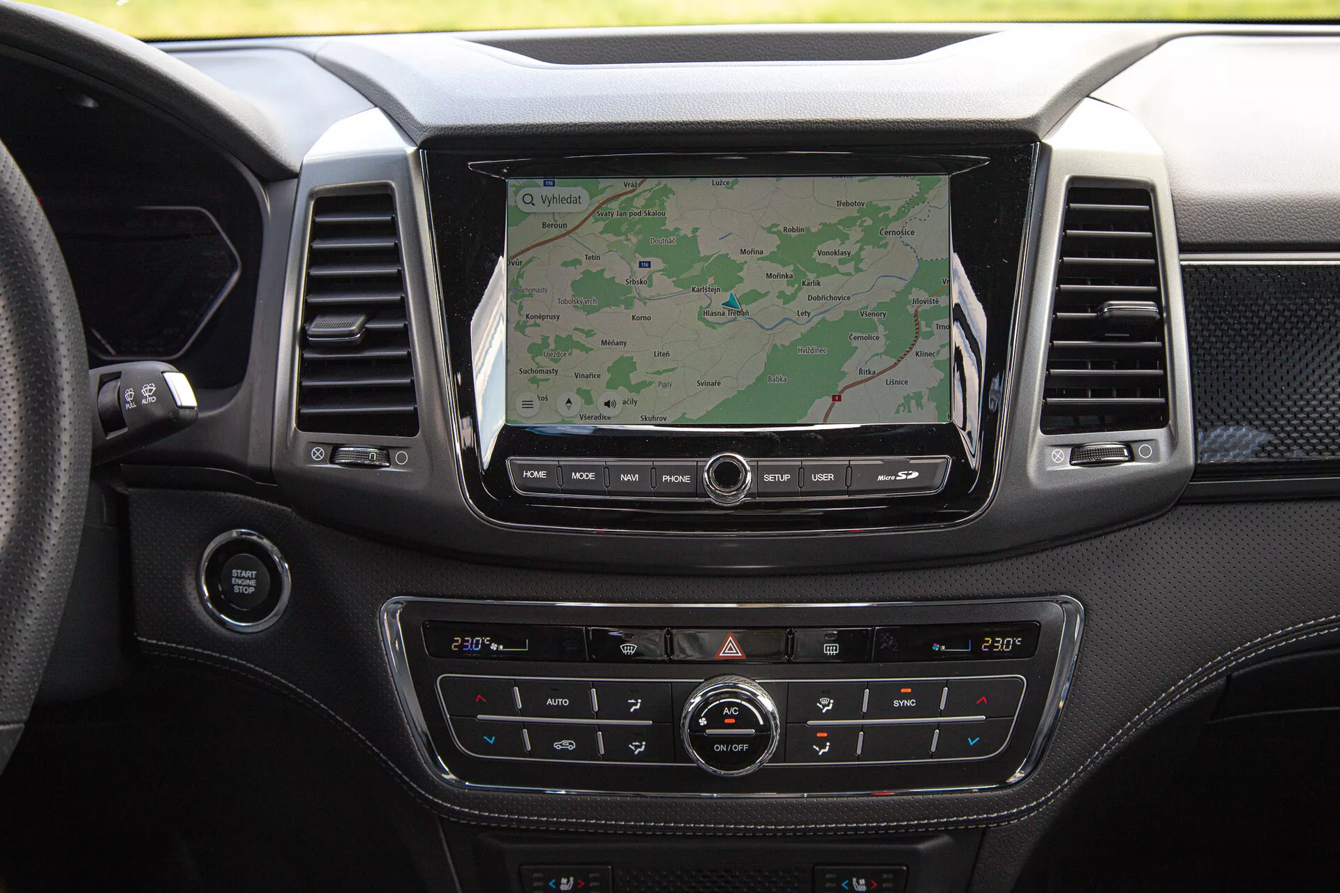 Palubní deska pick-upu SsangYong Musso Grand z roku 2022 s velkou obrazovkou infotainmentu zobrazující navigaci, duální klimatizaci, povrch z prémiového materiálu a různá ovládací tlačítka