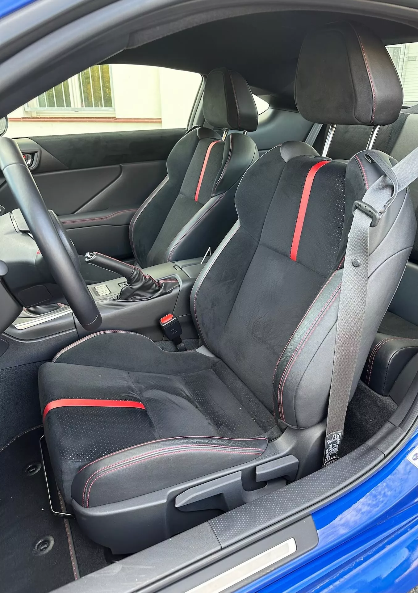 Interiér Subaru BRZ 2023 s důrazem na sportovní přední sedadla s ergonomickým designem a červenými detaily, volič automatické převodovky a moderní estetiku kokpitu z šikmé vnější perspektivy