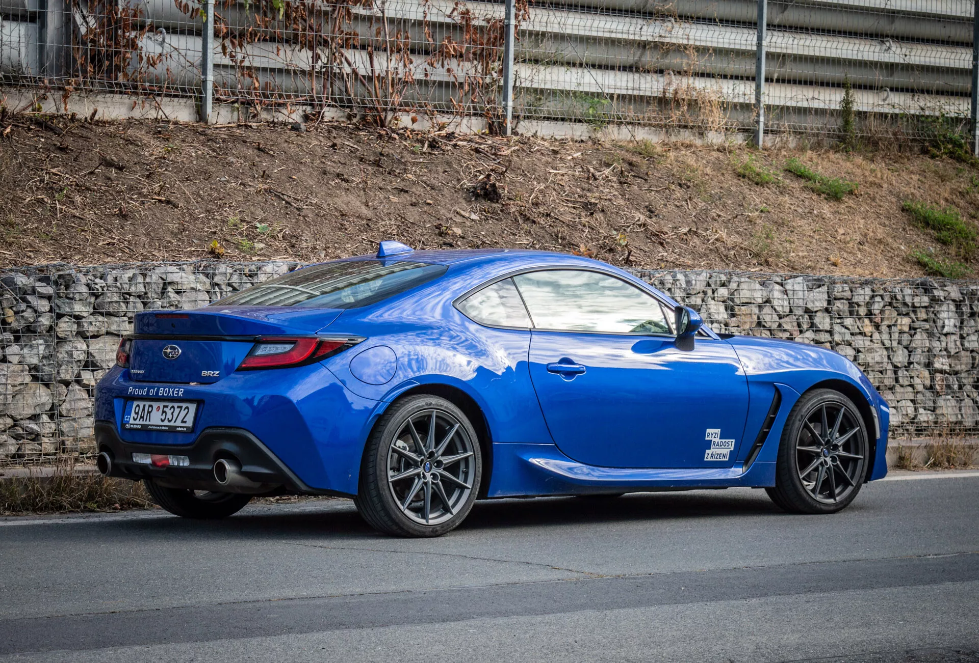 Světle modré sportovní kupé Subaru BRZ 2023 s aerodynamickým designem, zaparkované na ulici, s výrazným zadním blatníkem, zadními světly, zakřivením zadního okna směřujícím k viku zavazadlového prostoru, tvarovanými liniemi, klesající střechou, slitinovými koly s více paprsky, brzdami vysokého výkonu, nízko profilovým zadním spoilerem, dvojitými výfukovými trubkami v zadním difuzoru, zrcátky v barvě karoserie a sportovní dlouhou kapotou.