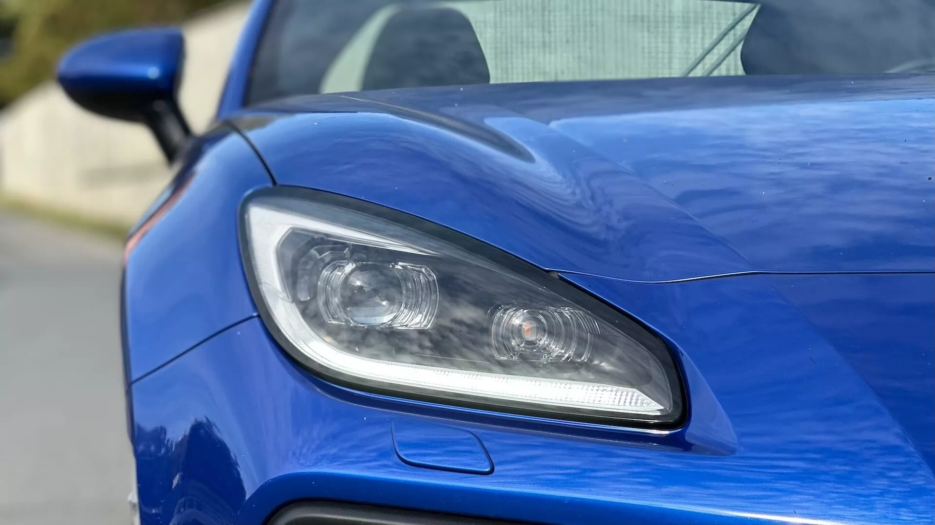 Detailní záběr na přední světlomet řidičovy strany Subaru BRZ 2023, zahrnující design LED nebo HID osvětlení, projekční čočky a sportovně laděný vzduchový vstup na metalické modré karoserii