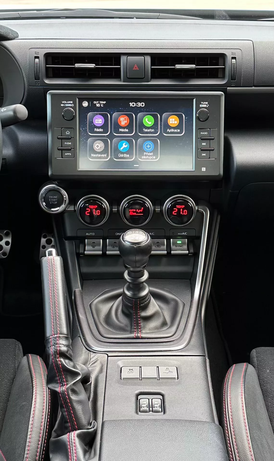 Interiér Subaru BRZ 2023 s pohledem na středovou konzolu, obsahující dotykovou obrazovku infotainmentu, indikátor výstražného světla, metalické vzduchové ventily, systém klimatizace pro obě zóny, manuální řadící páku s koženým manžetou, ovladače vyhřívání sedadel a selektor více režimů jízdy v moderním černém a metalickém designu.