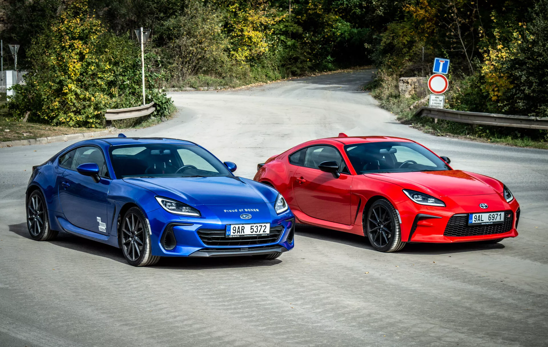 Duo Subaru BRZ 2023 předvádějící sportovní vozy ve stylu kupé v jasně modré a výrazné červené barvě zaparkované vedle sebe na asfaltu s aerodynamickými designovými prvky, moderními LED světlomety a koly orientovanými na výkon pod přirozeným denním světlem
