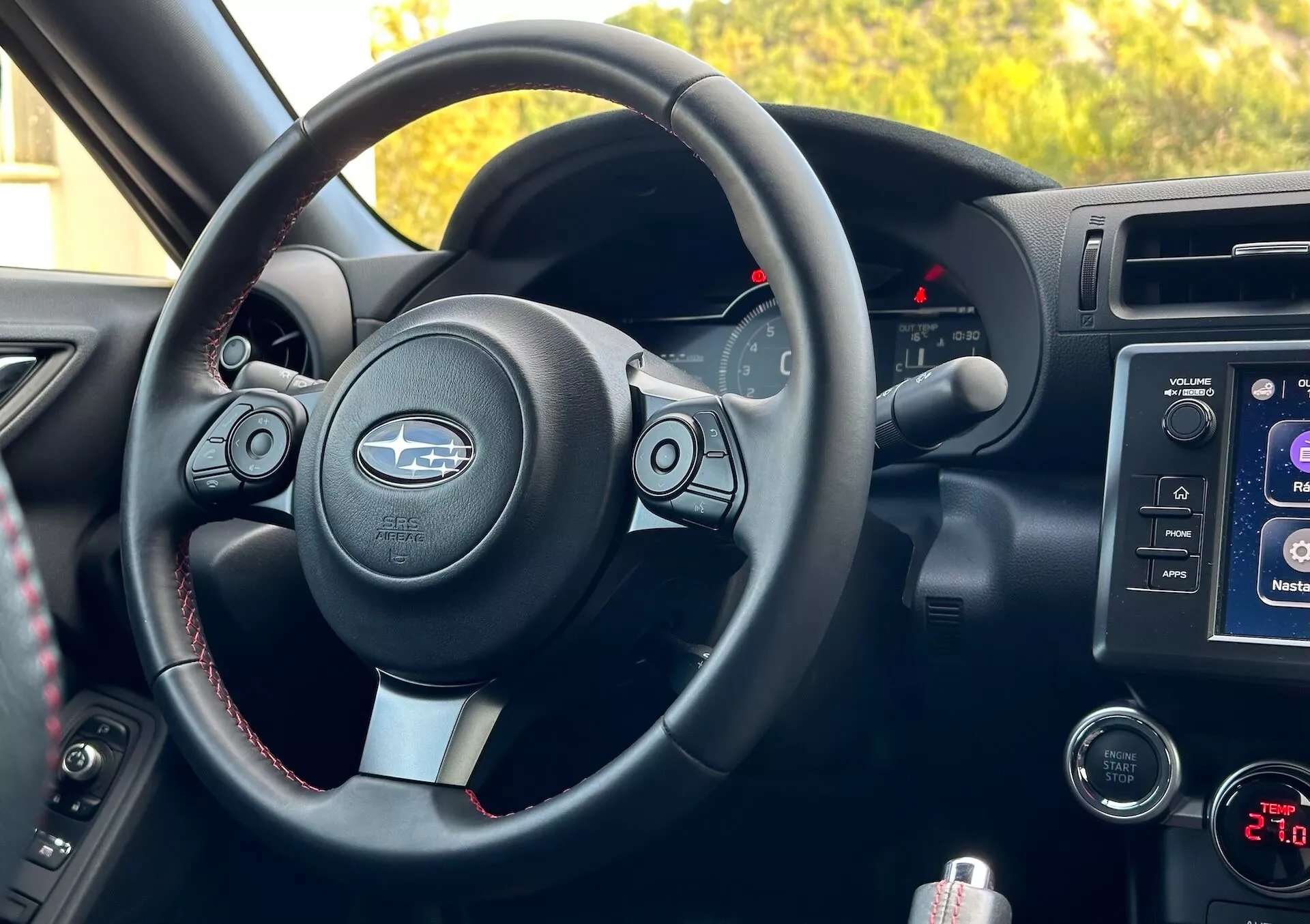 Interiér Subaru BRZ 2023 z pohledu spolujezdce s volantem s kovovými akcenty a logem Subaru, tlačítky ovládání, kontrastním prošíváním, přístrojovou deskou s podsvícenými ukazateli, centrálním konzolovým infotainment systémem, ovládáním audia a klimatizace a odkládacím prostorem.