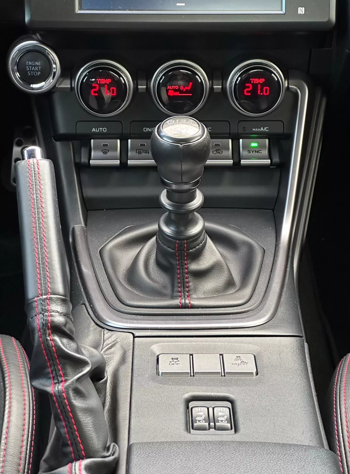 Centrální konzola Subaru BRZ 2023 s manuální převodovkou se sportovní červenou stehováním, pomocnými měřiči pro tlak turbodmychadla, napětí baterie, teplotu oleje a duální klimatizací v detailním pohledu interiéru