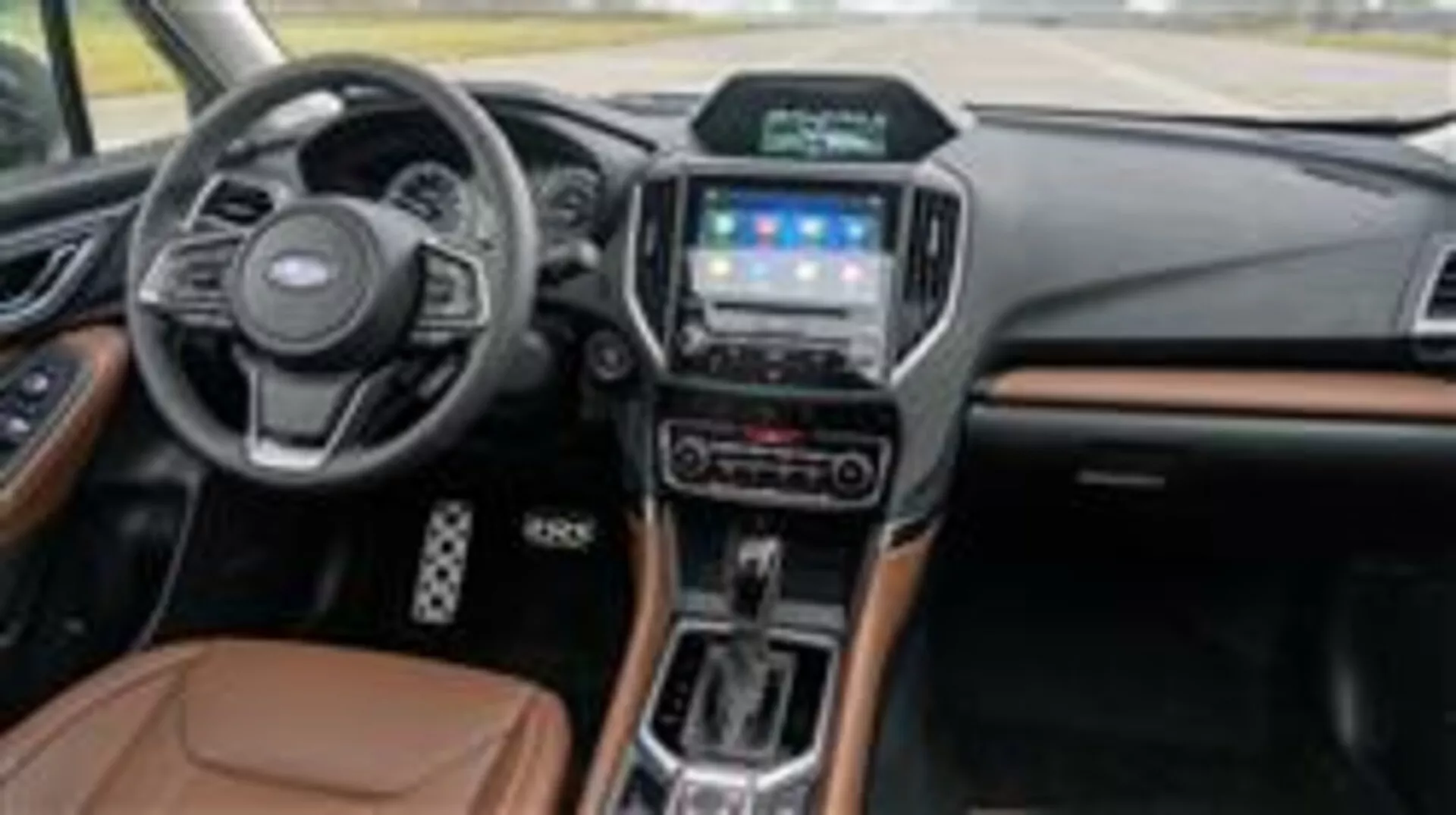 Interiér Subaru Forester 2015 s palubní deskou, multifunkčním volantem, dotykovým informačním systémem, voličem automatické převodovky a luxusními materiálovými akcenty z pohledu spolujezdce