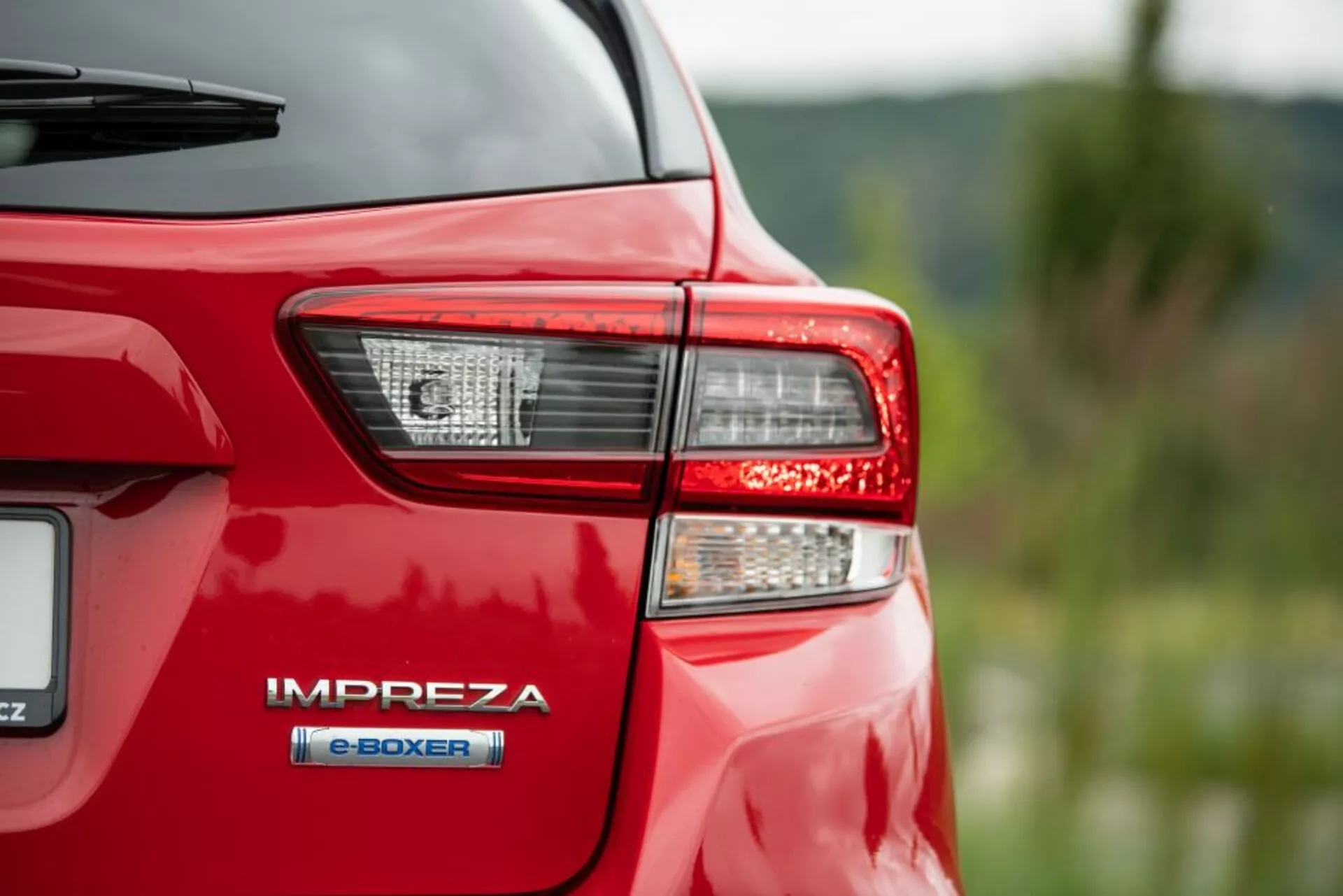 Detailní záběr zadního rohu červeného Subaru Impreza z roku 2018, zaměřený na zadní světlo a odznak s hybridním motorem 'e-BOXER', zdůrazňující pokročilou hybridní technologii a LED osvětlení Subaru