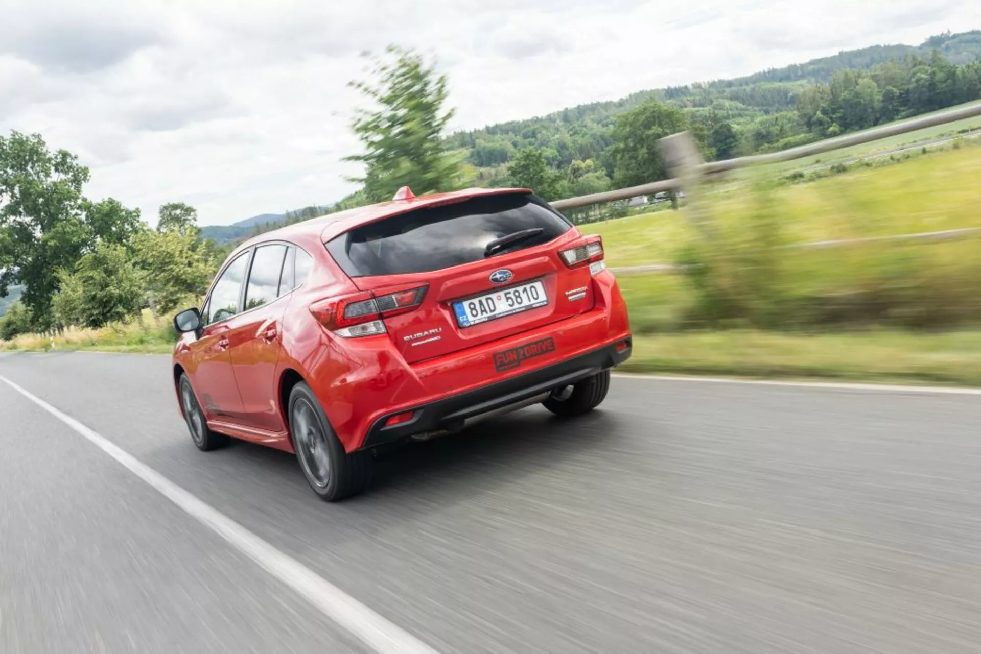 Subaru Impreza 2018 v jasně červené barvě, která zdůrazňuje moderní design s aerodynamickým zadním spoilerem a dvojitým výfukem, zachycen z úhlu tři čtvrtě zadní části, což zdůrazňuje rychlost a linie designu.