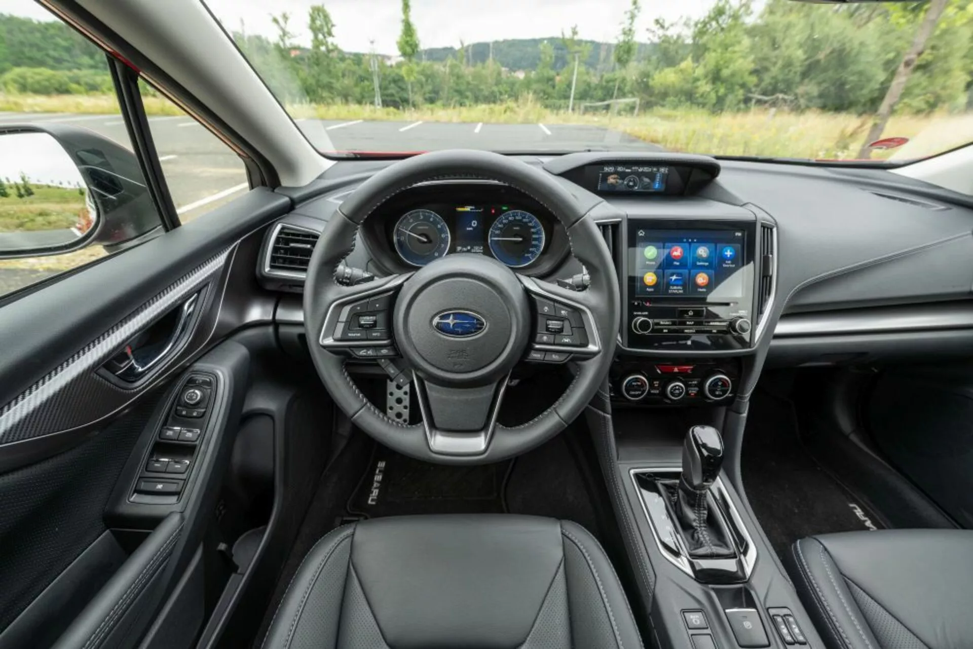 Interiérový pohled na Subaru Impreza 2018 ukazující perspektivu řidiče na palubní desku, středovou konzolu, multifunkční volant, dotykový infotainmentový systém, řadicí páku automatické převodovky a sedadla potažená kůží