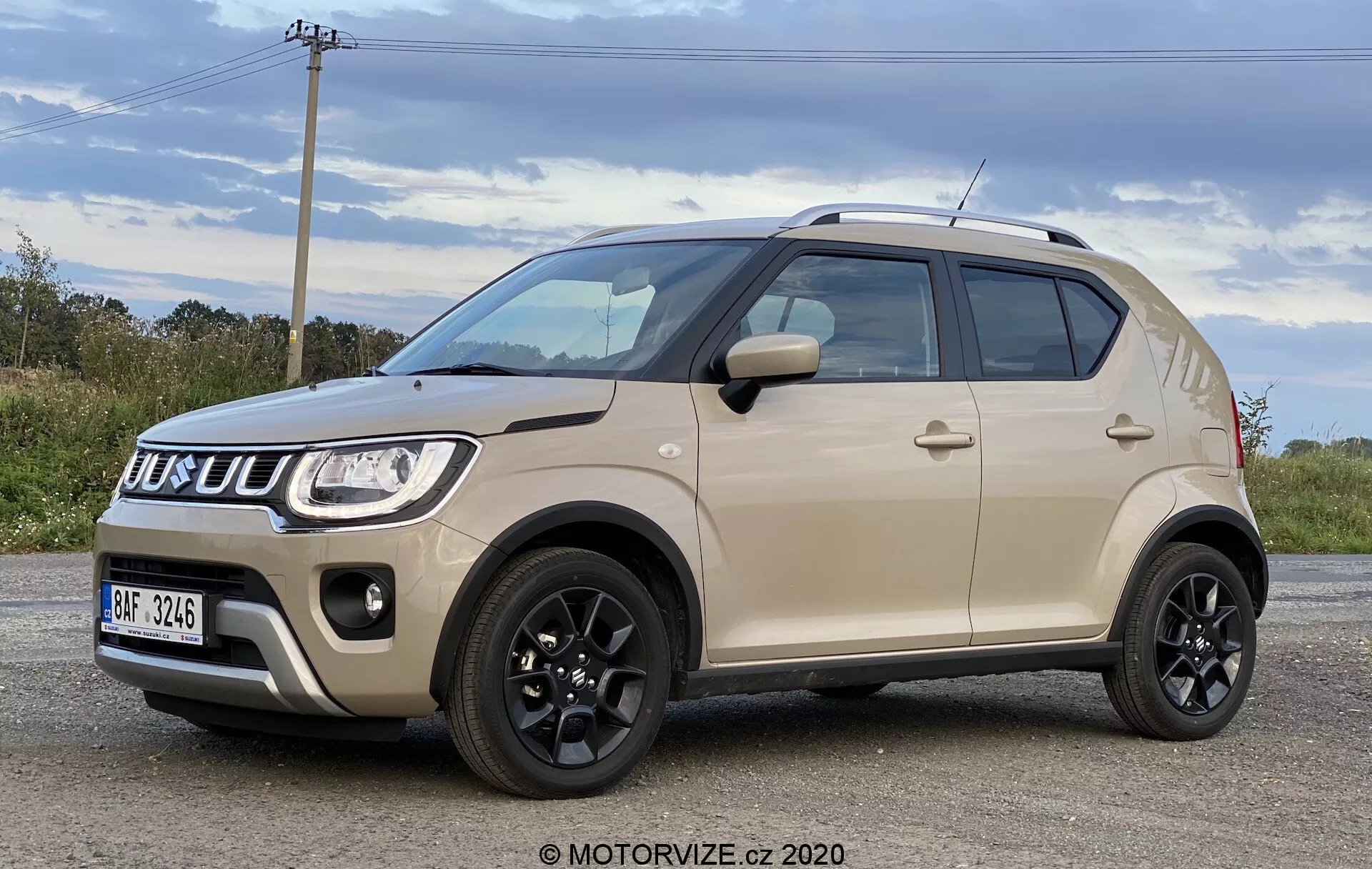Tříčtvrteční pohled zepředu na Suzuki Ignis 1.2 Dualjet Hybrid Club 2020, ukazující jeho současný kompaktní SUV design s dvoubarevným karoserií, výraznou mřížkou a světlomety a robustními koly. Moderní estetiku vozidla zvýrazňuje černá střecha, zrcátka, boční lišty a velké nízkoprofilové pneumatiky, to vše ukazuje na vysokou světlou výšku vhodnou pro různorodé podmínky jízdy.